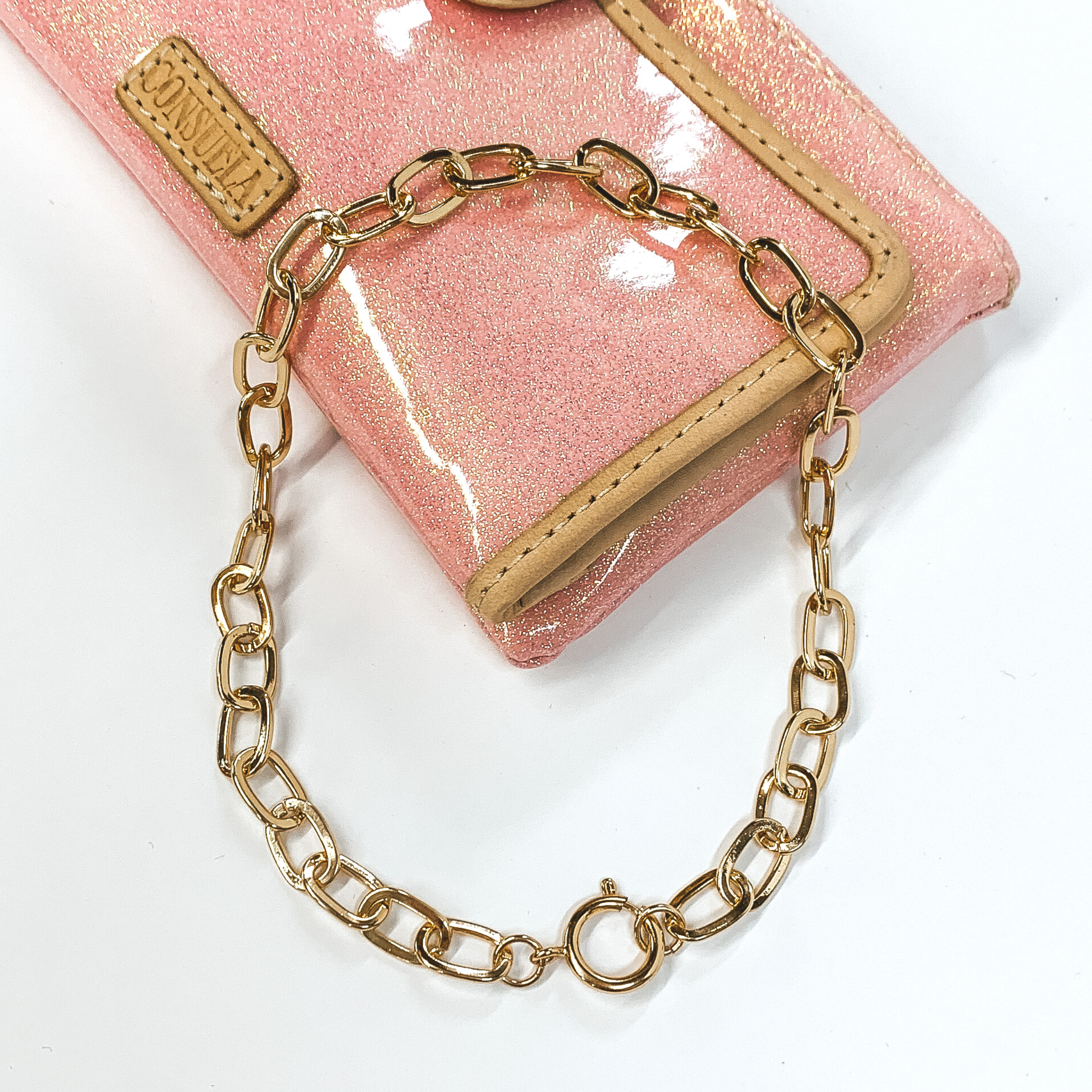 Paperclip gold chain necklace with a spring ring clasp. This necklace is pictured on a white and sparkle pink background. 