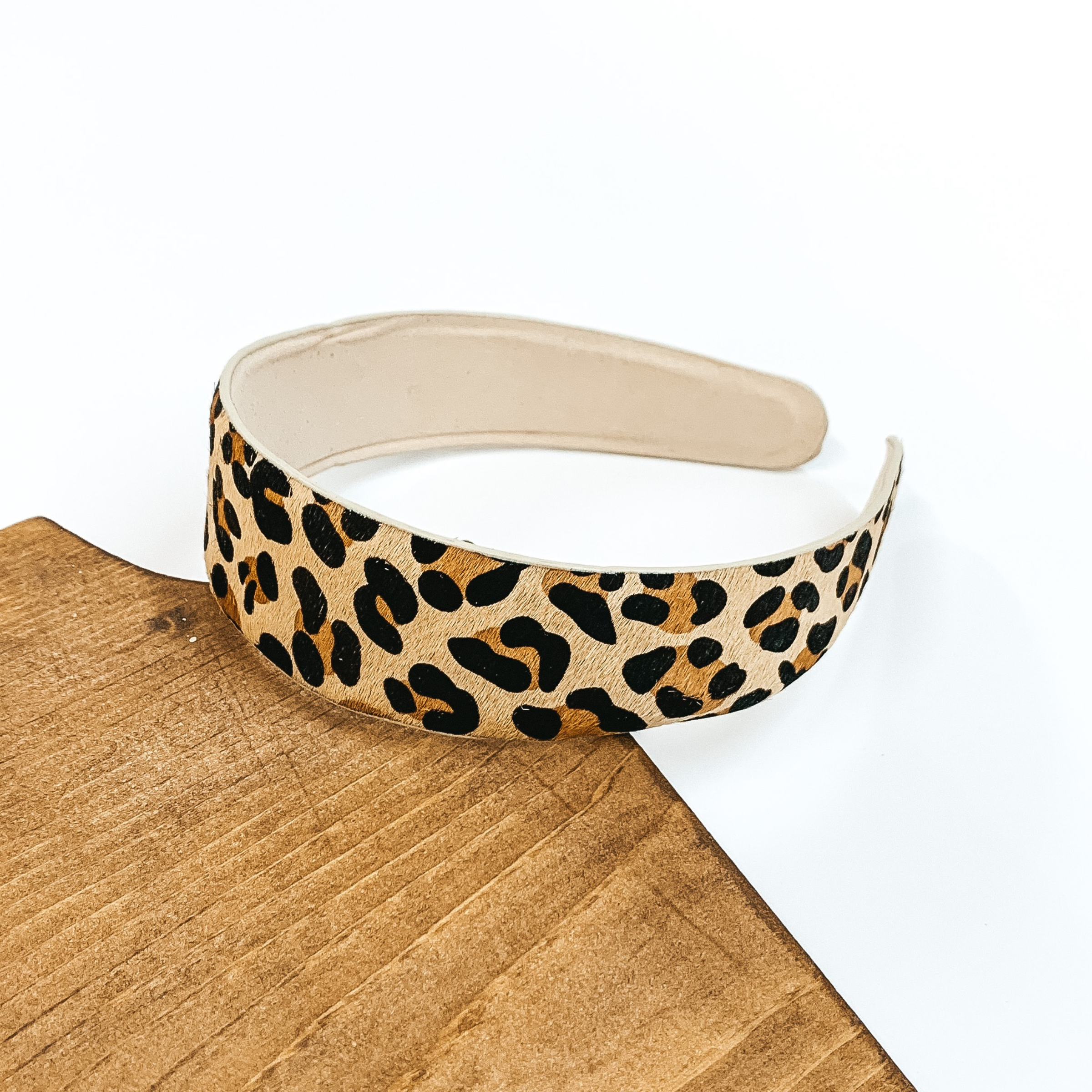 Leopard print headband and an ivory underside. This headband is pictured laying partially on some dark wood on a white background.