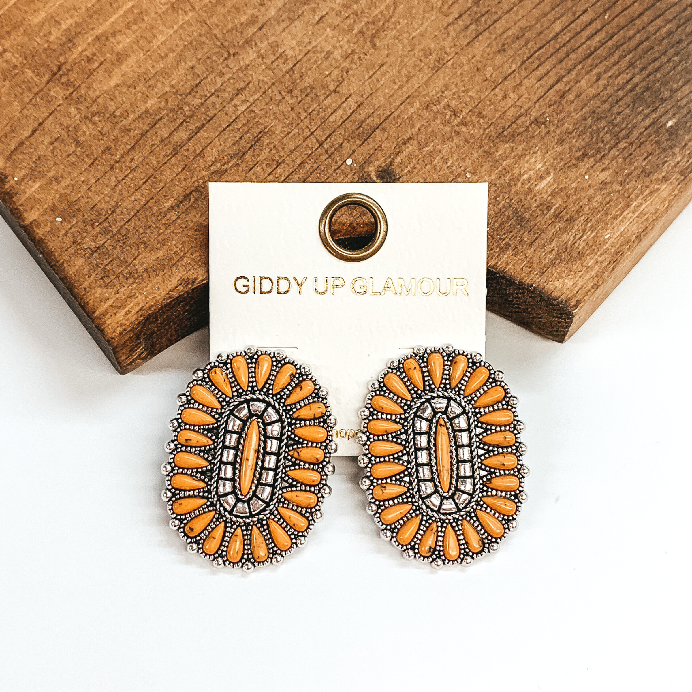 Mustard yellow stone cluster earrings in an oval shape. These earrings are pictured leaning against a brown block on a white background.