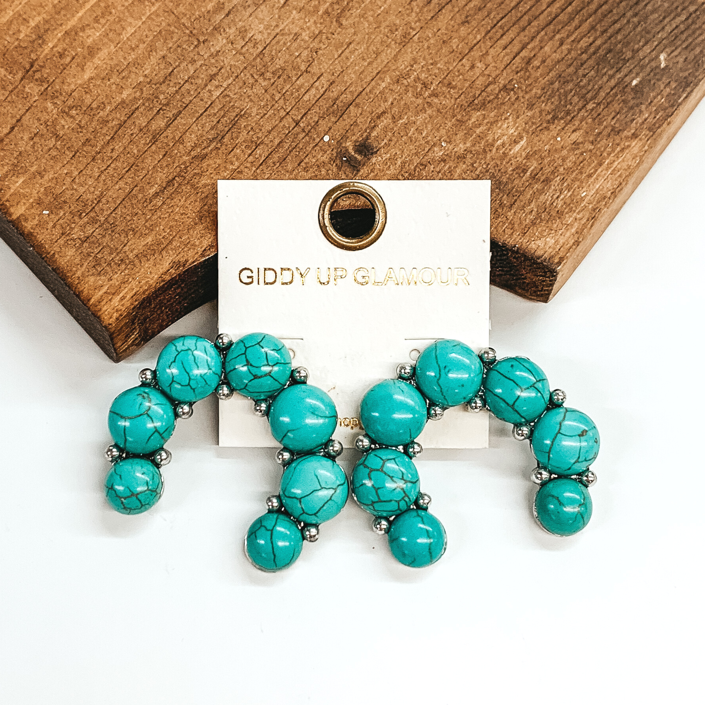Naja earrings with turquoise stones. These earrings are pictured leaning against a brown block on a white background.