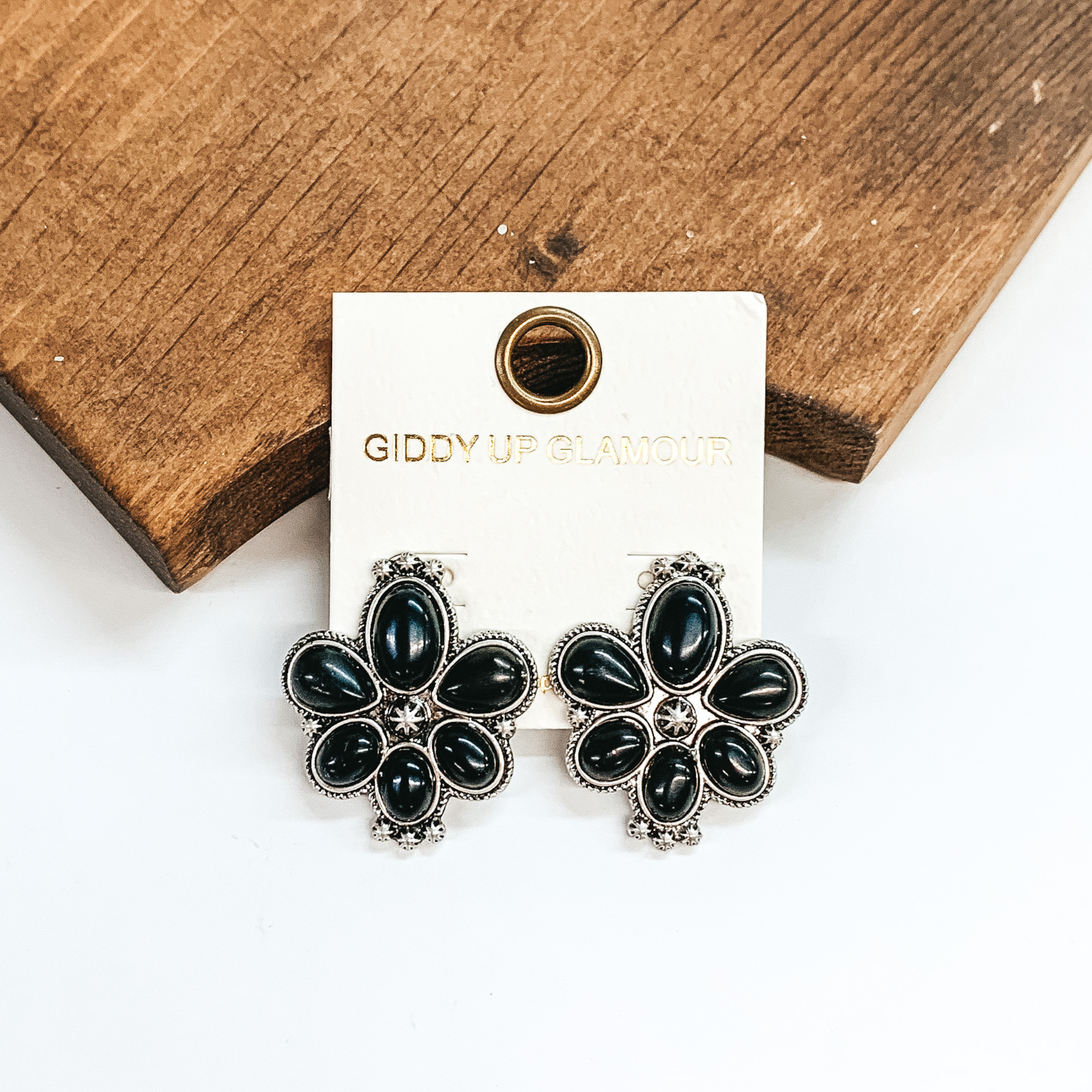 Six black stone cluster earrings. These earrings are pictured leaning against a brown block on a white background.