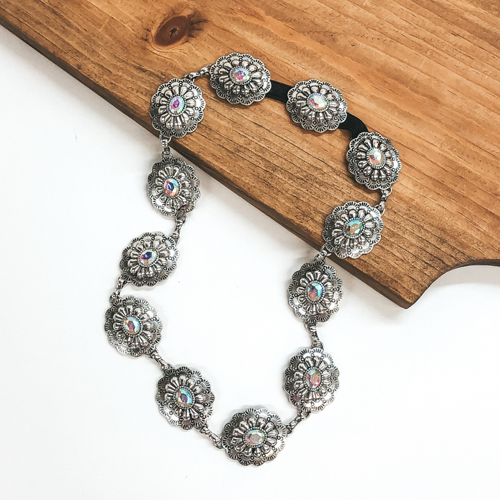 Silver, large oval concho hat band with large, center ab crystals. This hat band is pictured partially laying on a brown block on a white background.