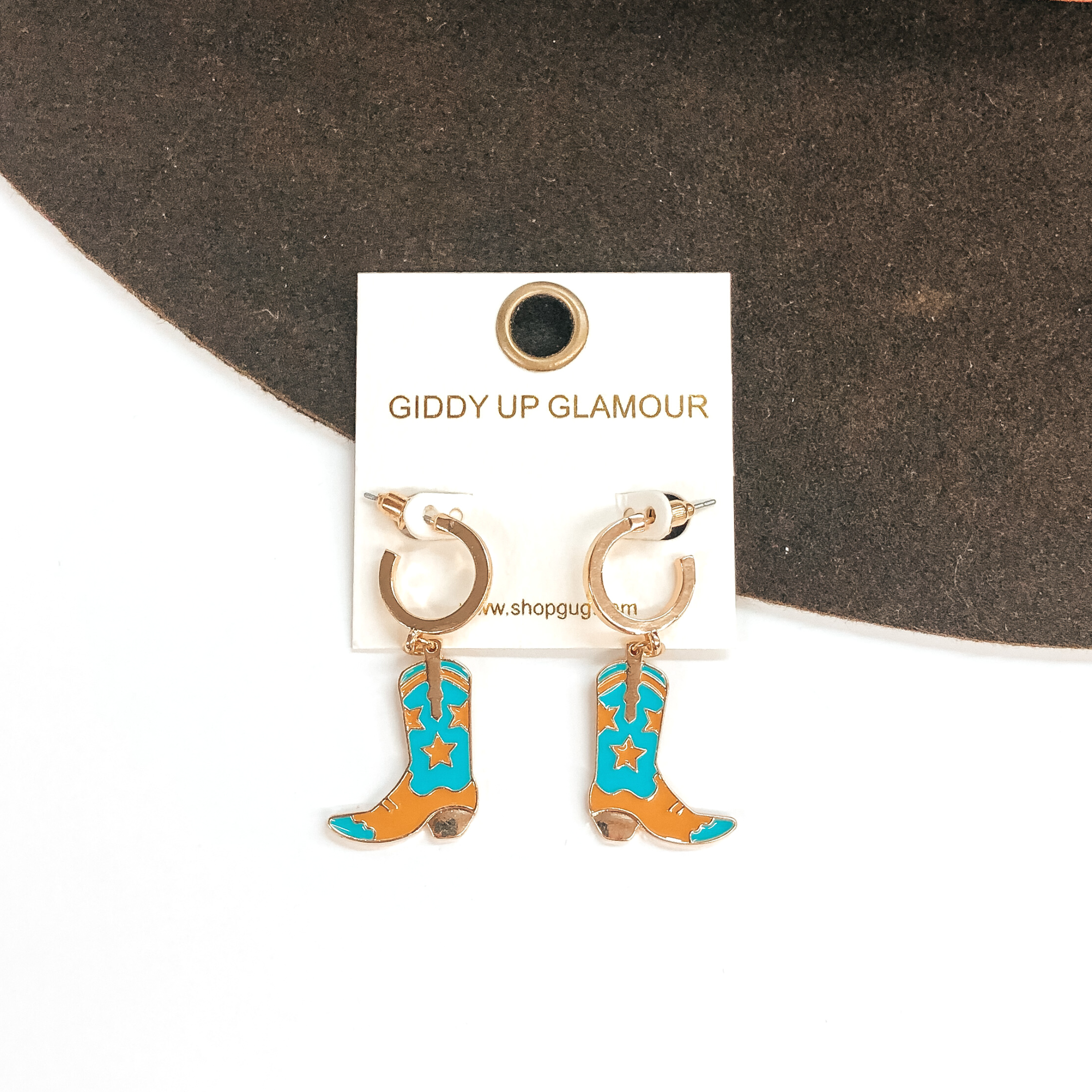Small gold hoop earrings with a turquoise and tan boot pendant hanging from the bottom. These earrings are pictured on a white and brown background. 