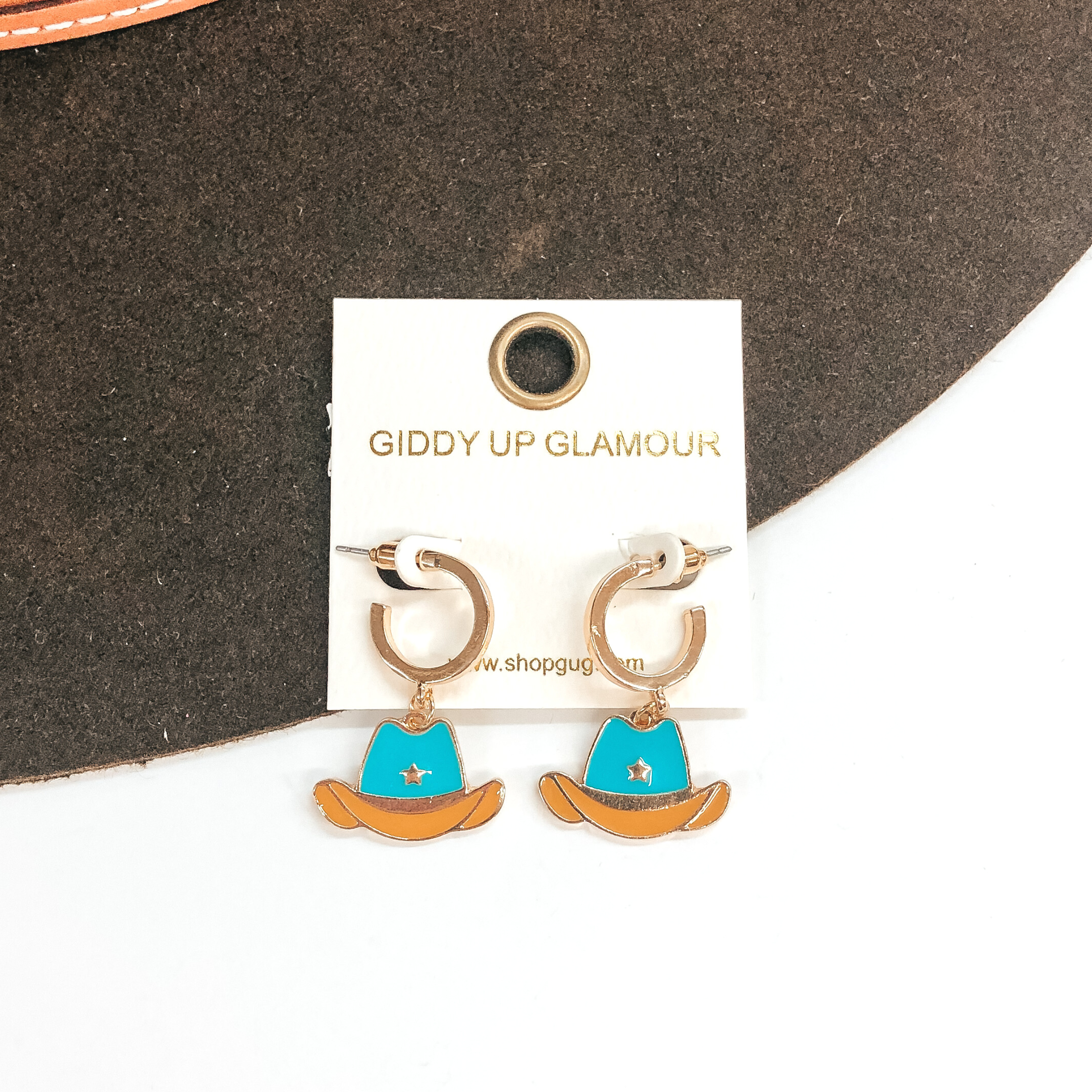 Small gold hoop earrings with a turquoise and tan hat pendant hanging from the bottom. These earrings are pictured on a white and brown background. 