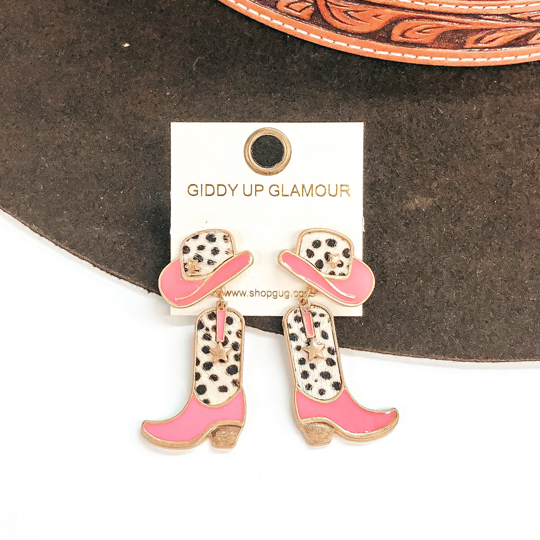 Hat stud earrings with a boot pendant drop. Both have a white and black dotted print with pink on the hat brim and on the foot part on the sock. These earrings are pictured on a white and brown background. 