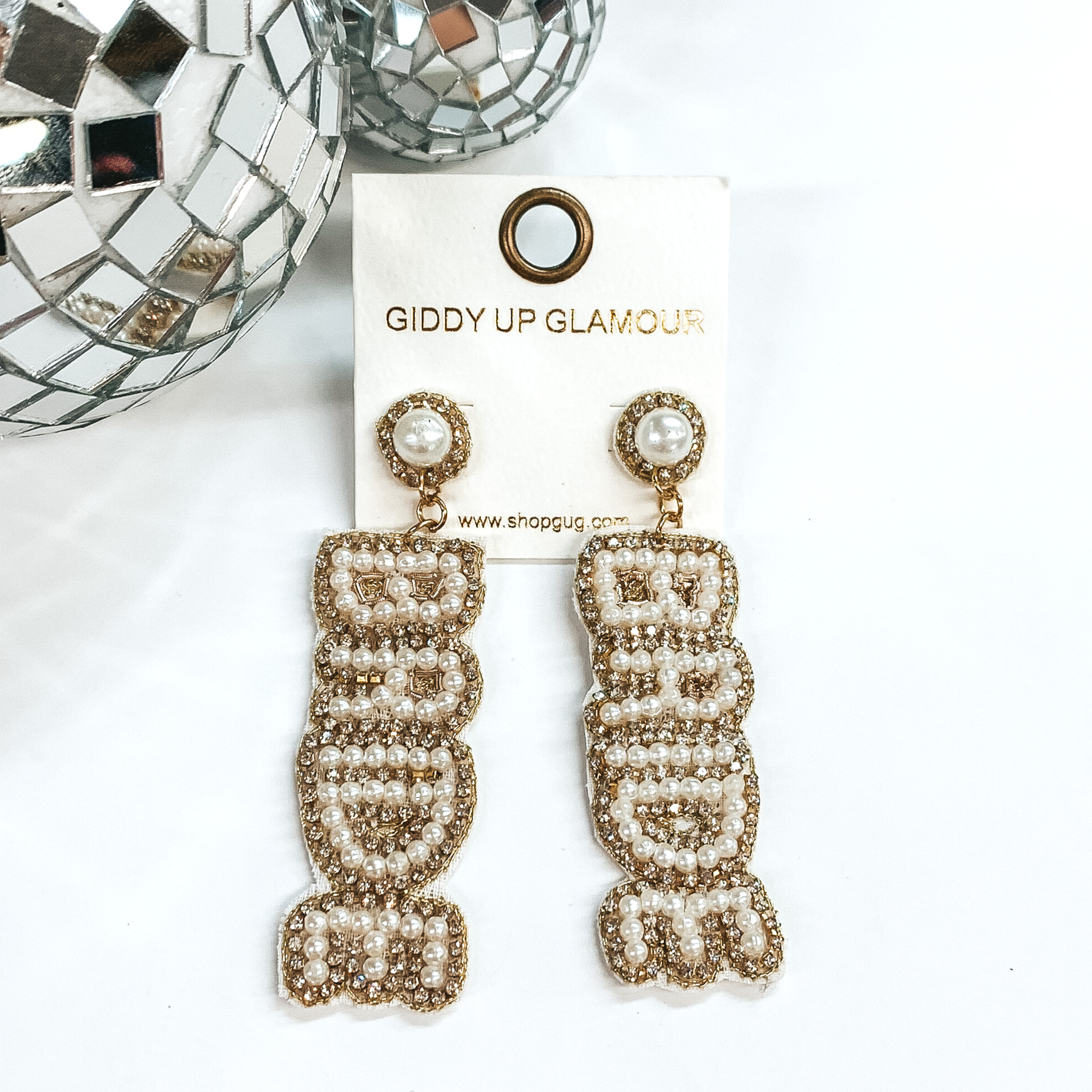 These earrings have pearl studs with a drop pendant with the word "BRIDE" spelled out in pearls. These earrings are also outline with clear crystals. This set of earrings are pictured on a white card holder on a white background with disco balls pictured on the top left corner. 