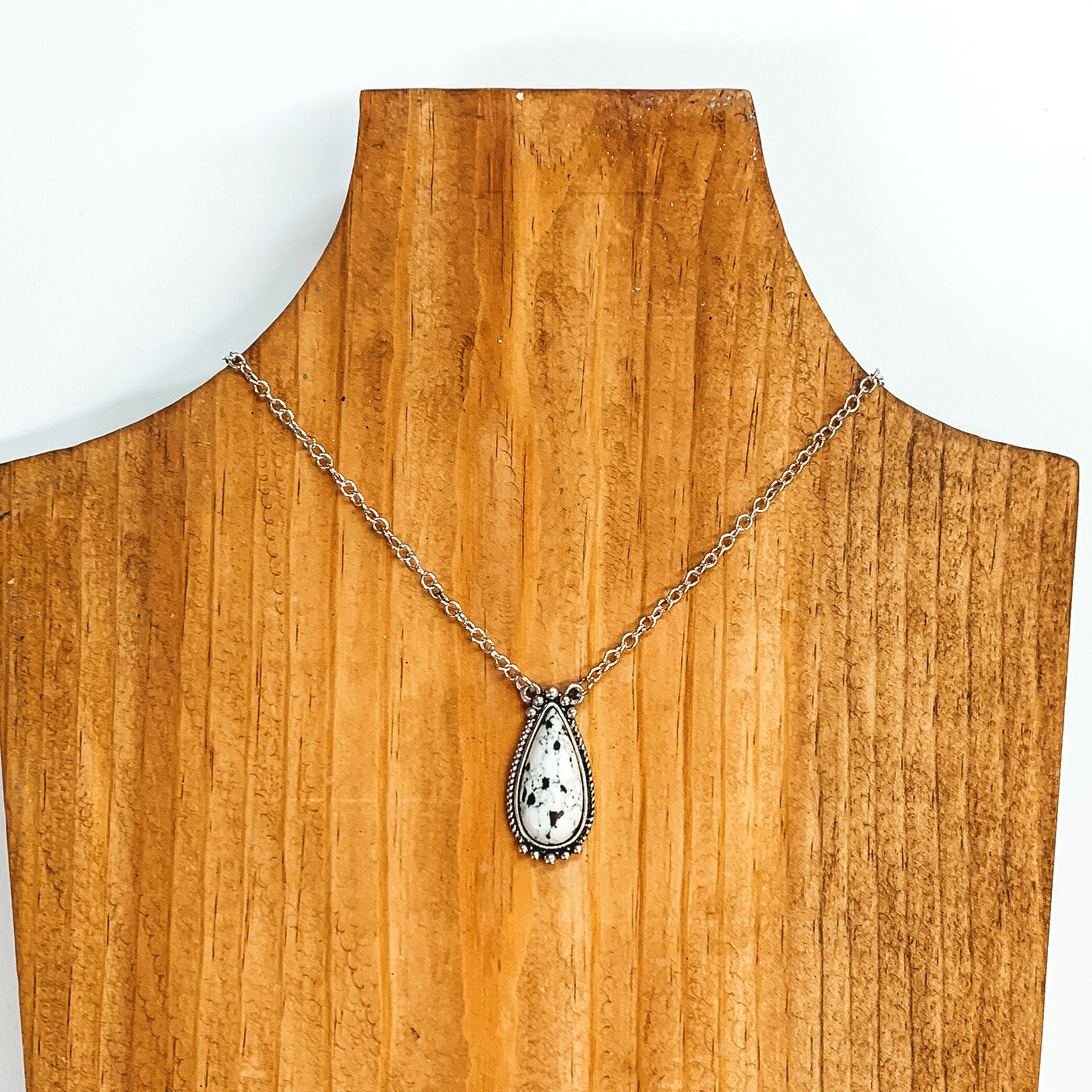 Silver chain necklace with a white teardrop pendant with a silver outline. This necklace is pictured on a wood necklace holder on a white background. 