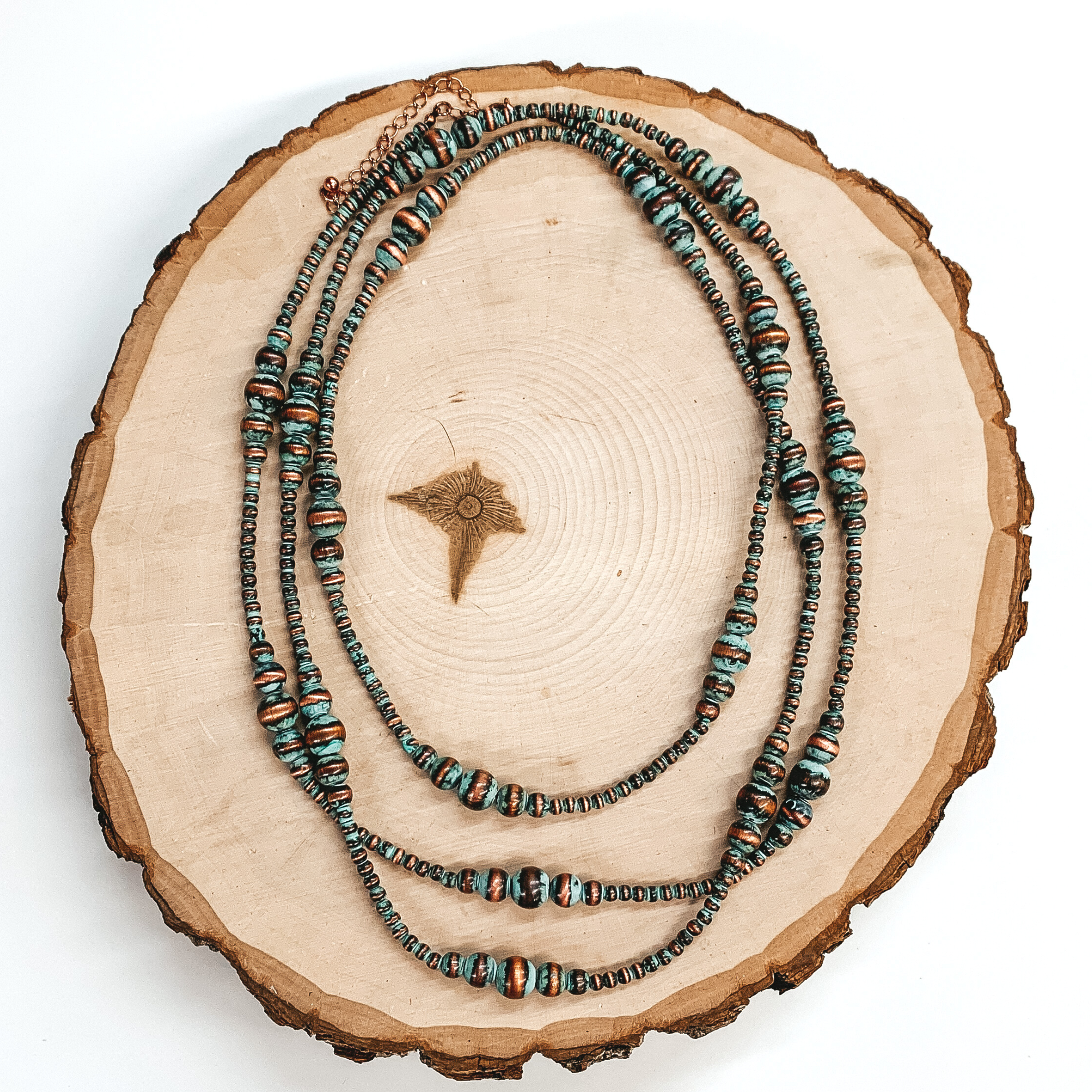 Patina beaded necklace with spacers of graduated pearls. This necklace is pictured laying on a cut block of wood on a white background. 