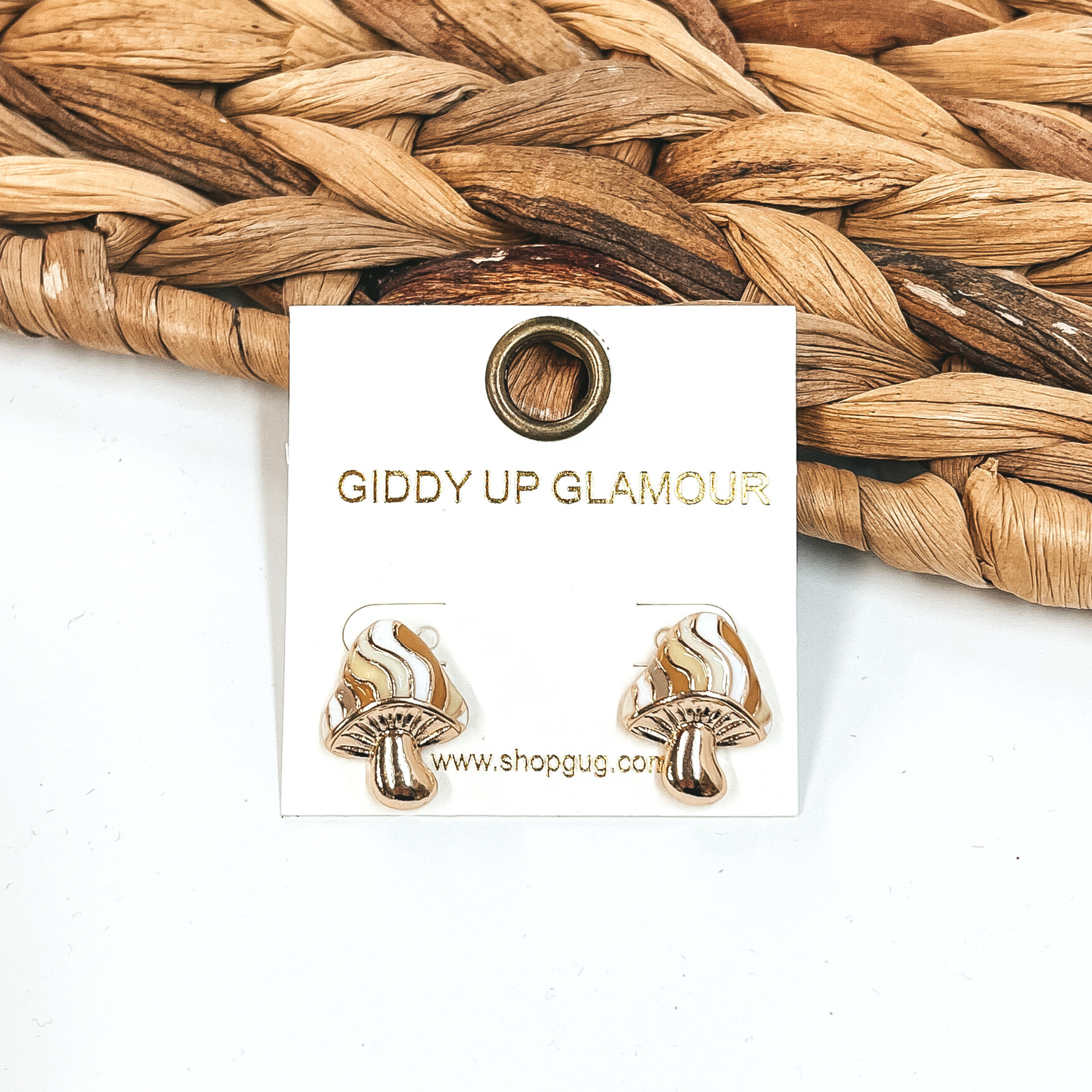 Gold, mushroom shaped earrings. The top part of the mushroom has different shades of ivory stripes. These earrings are pictured in front of a basket weave material on a white background.