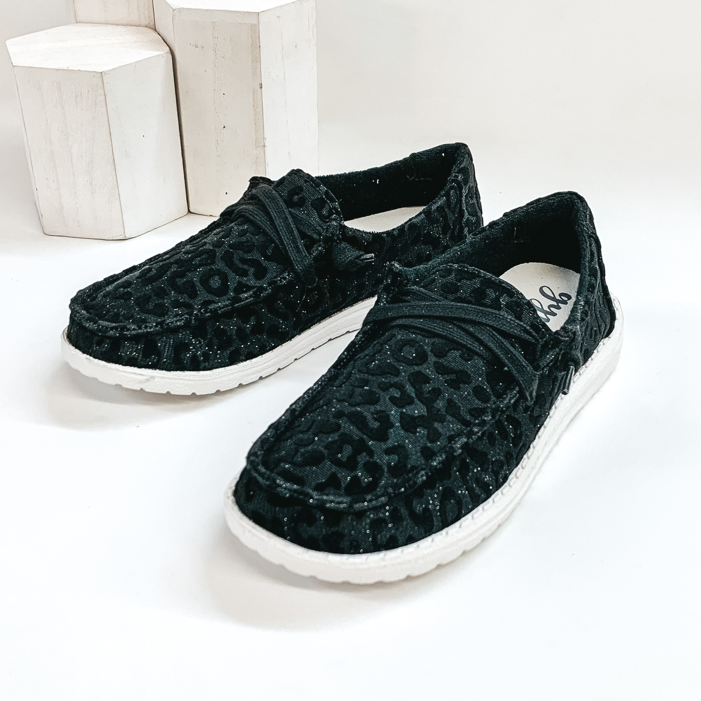 A pair of glitter black leopard print lace up loafers pictured on white background with white blacks behind them. .
