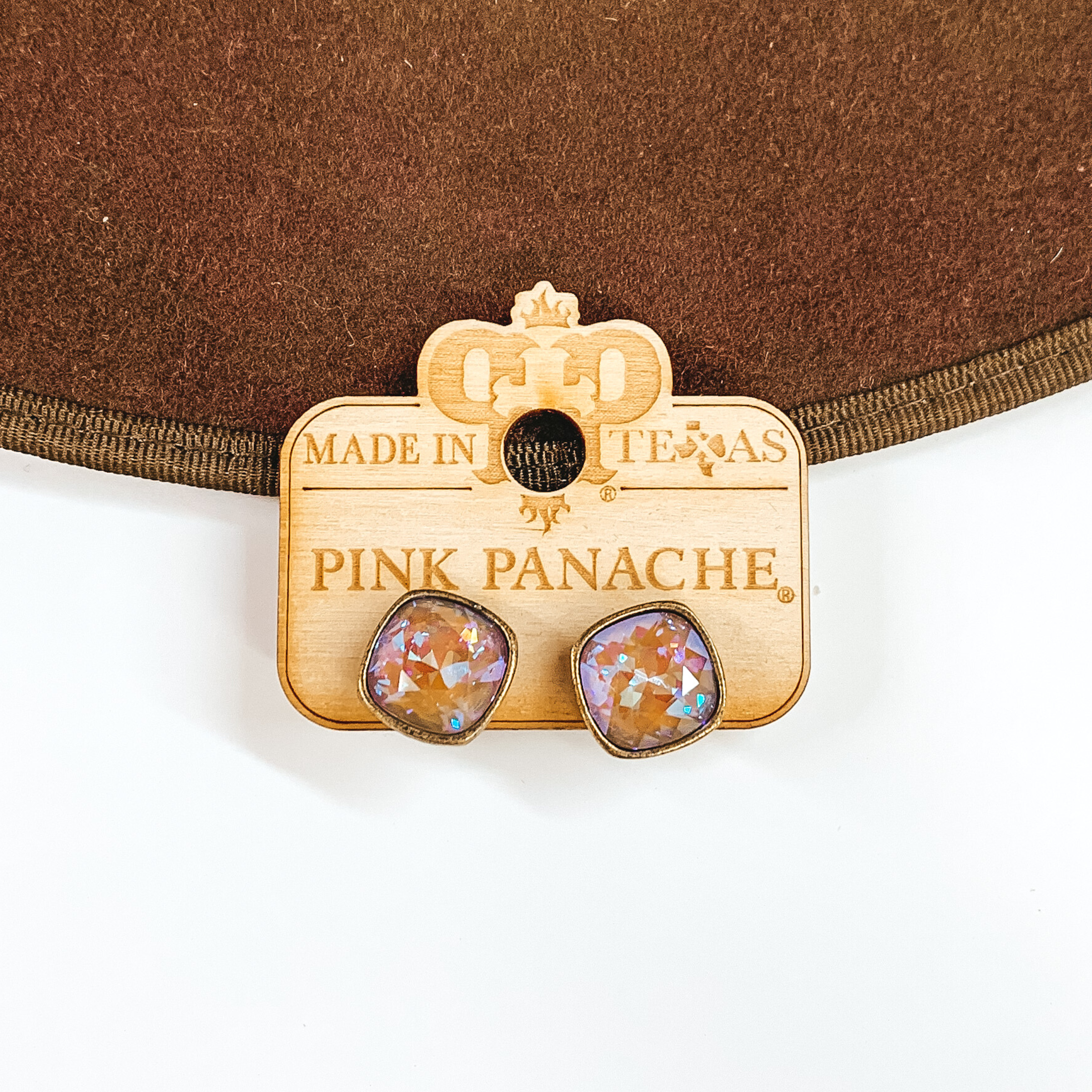 A pair of bronze earrings with cappuccino delight cushion cut crystals. These earring are pictured on a wood holder on a white and brown background.