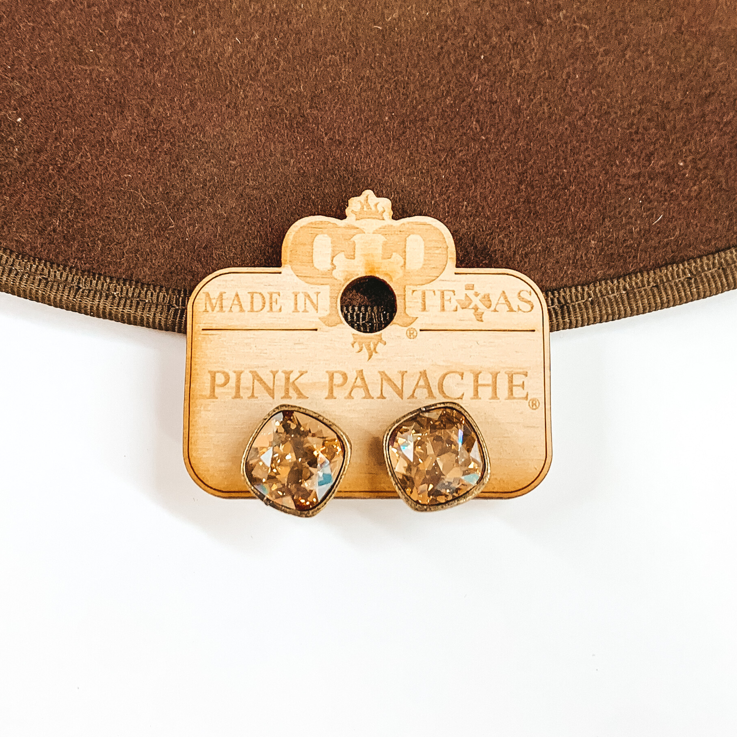A pair of bronze earrings with golden shadow cushion cut crystals. These earring are pictured on a wood holder on a white and brown background. 