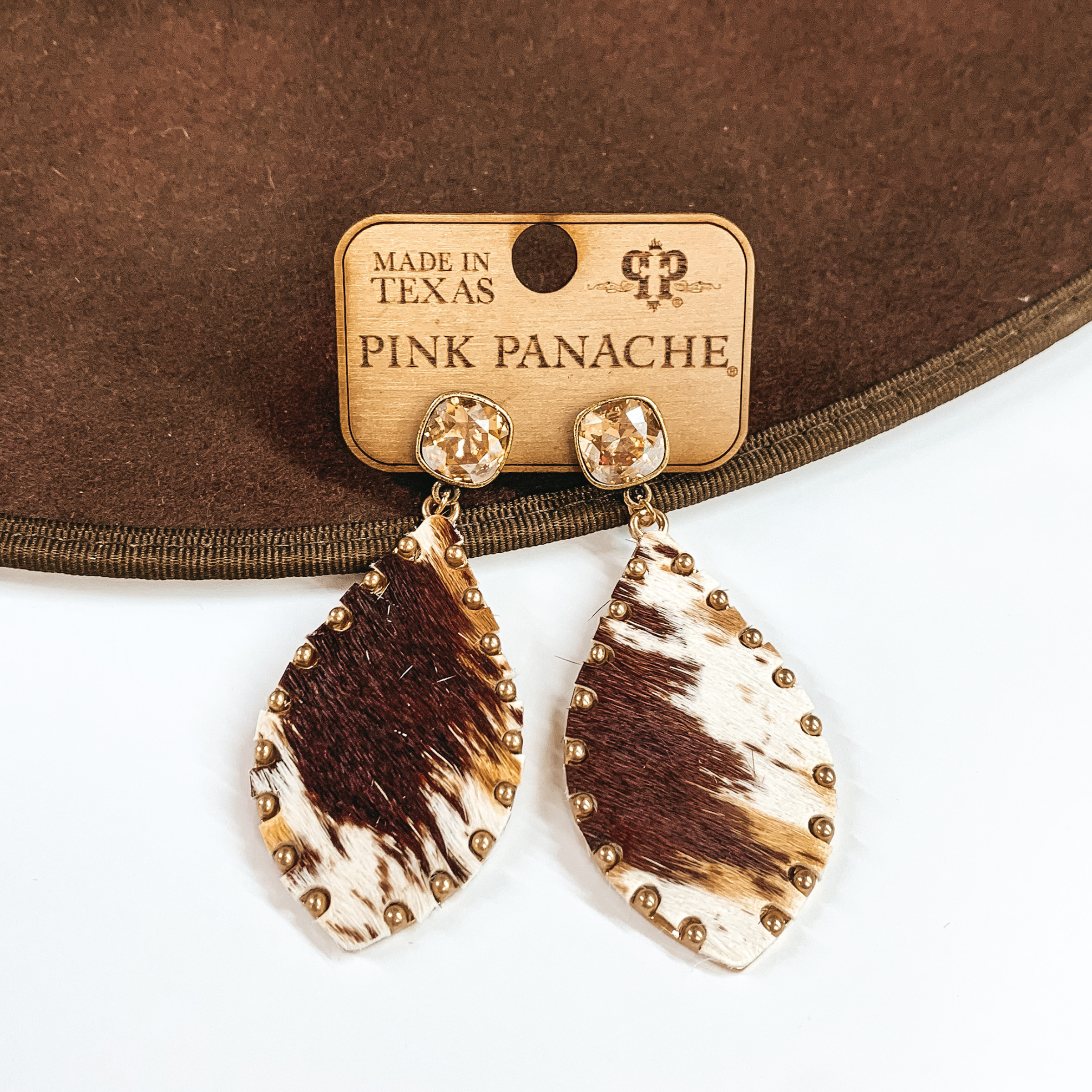 Pair of brindle print teardrop earrings with golden shadow cushion cut crystal stud earrings. These earrings are pictured laying partially on a brown hat brim on a white background.
