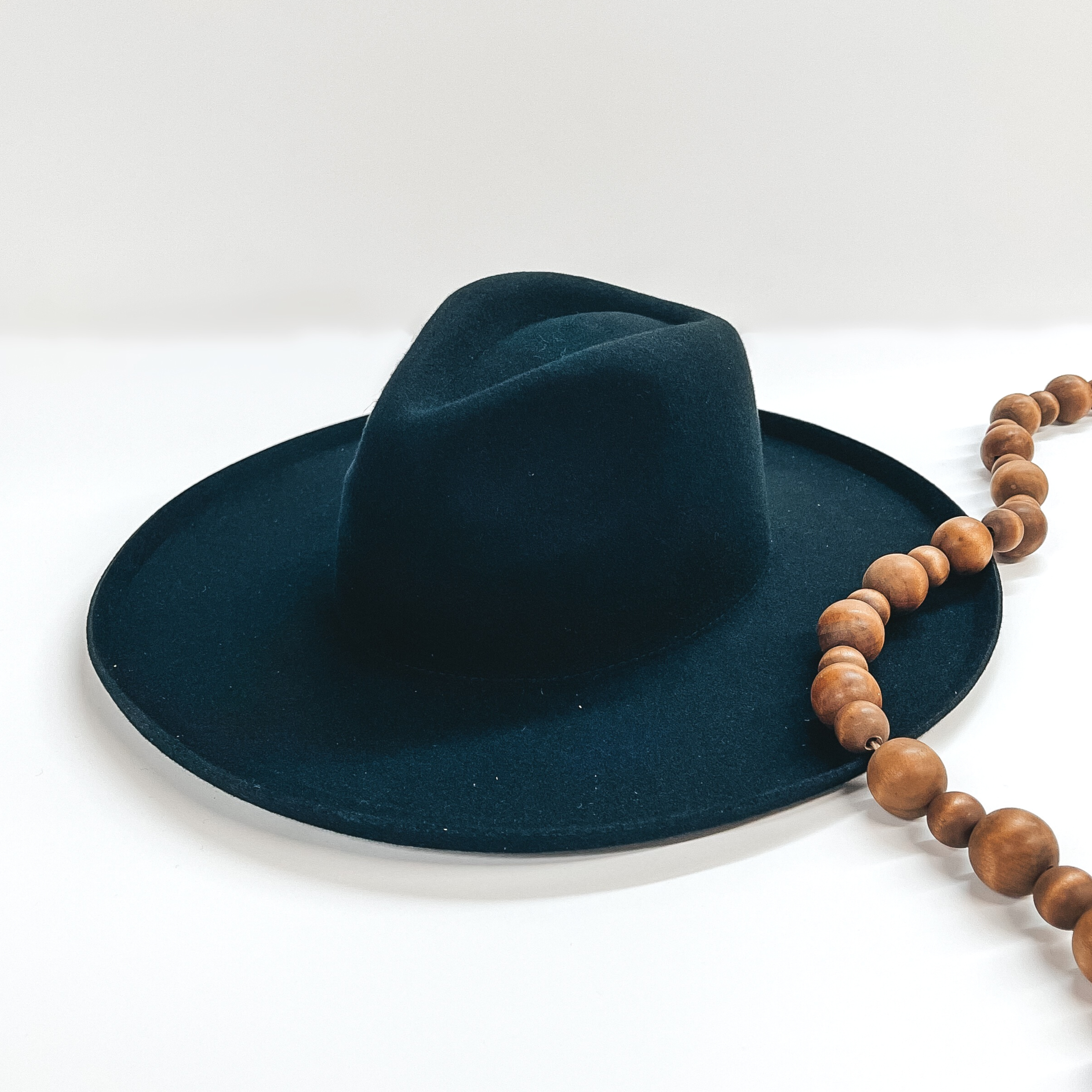 Black felt hat with a triangle top and a flat rbim with a flipped up edge. This hat is pictured on a white background with brown decorative beads. 