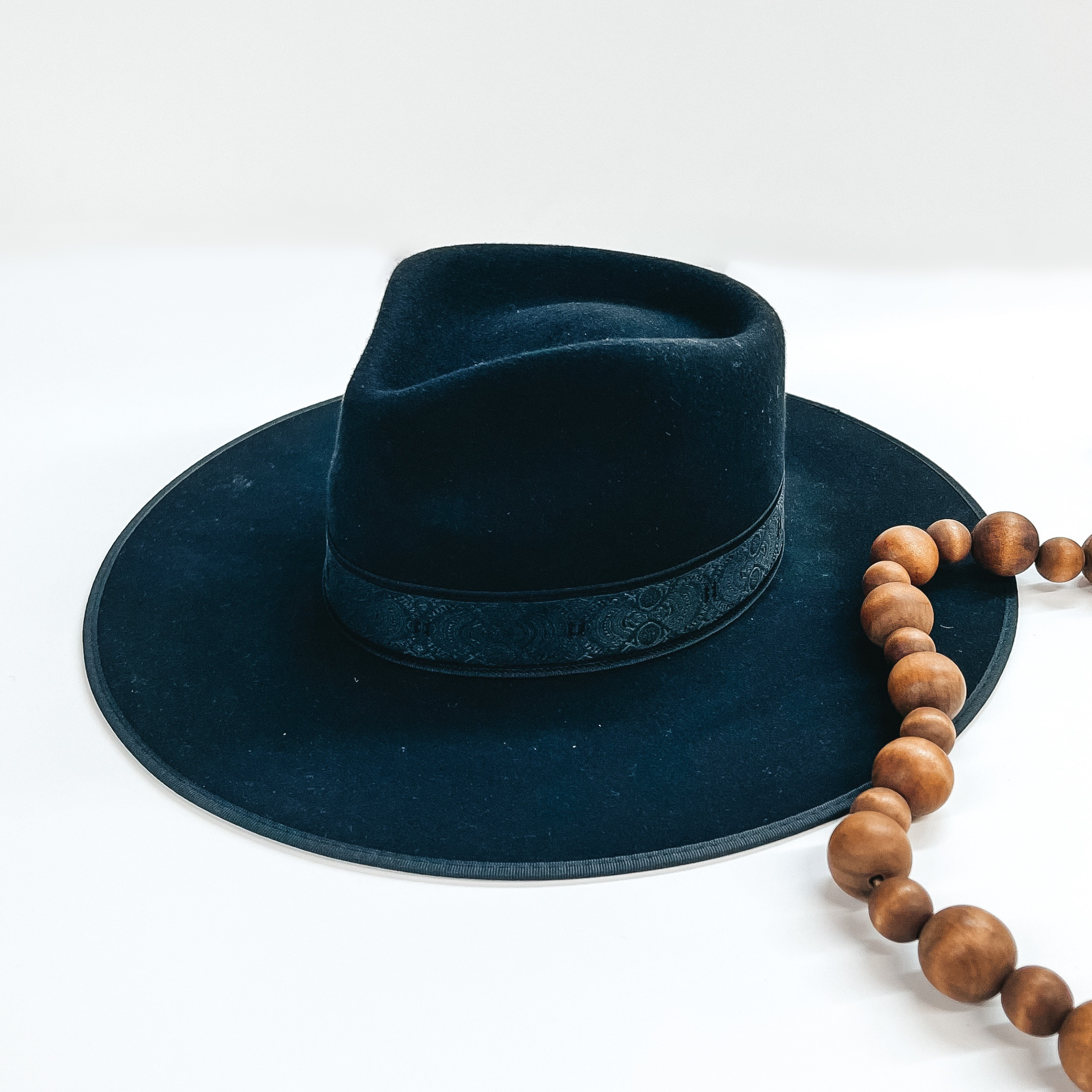 Black felt hat with a structured top and a flat brim. This hat also has a light black lace hat band. This hat is pictured on a white background with brown decorative beads. 