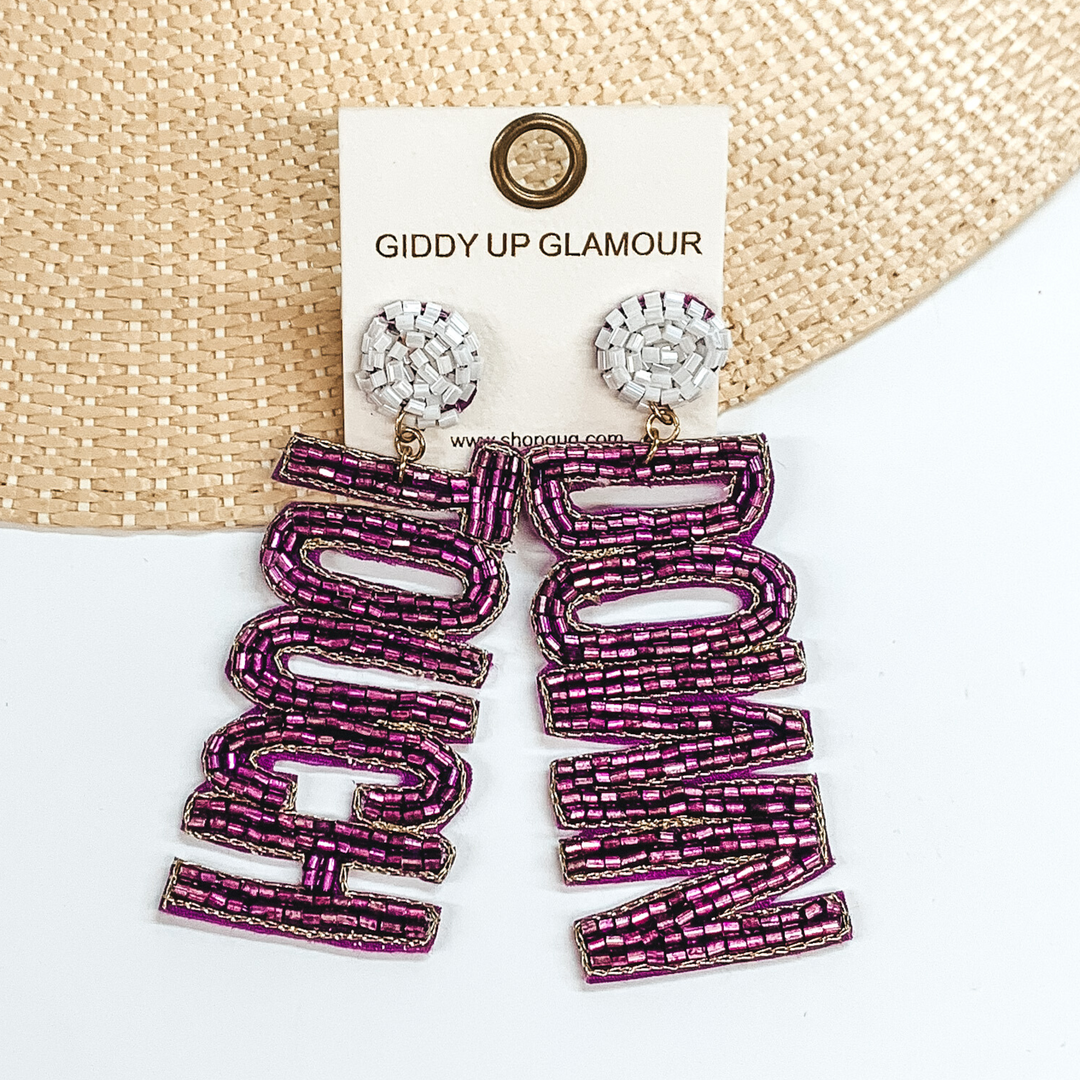 White beaded circle post back earrings. These earrings include the words "Touch" and "Down" in purple beads. These earrings are pictured partially laying on a straw hat brim on a white background. 