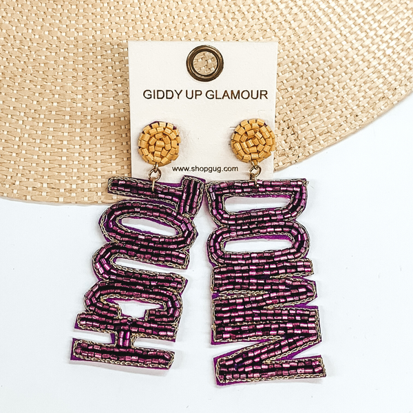 Mustard beaded circle post back earrings. These earrings include the words "Touch" and "Down" in purple beads. These earrings are pictured partially laying on a straw hat brim on a white background. 