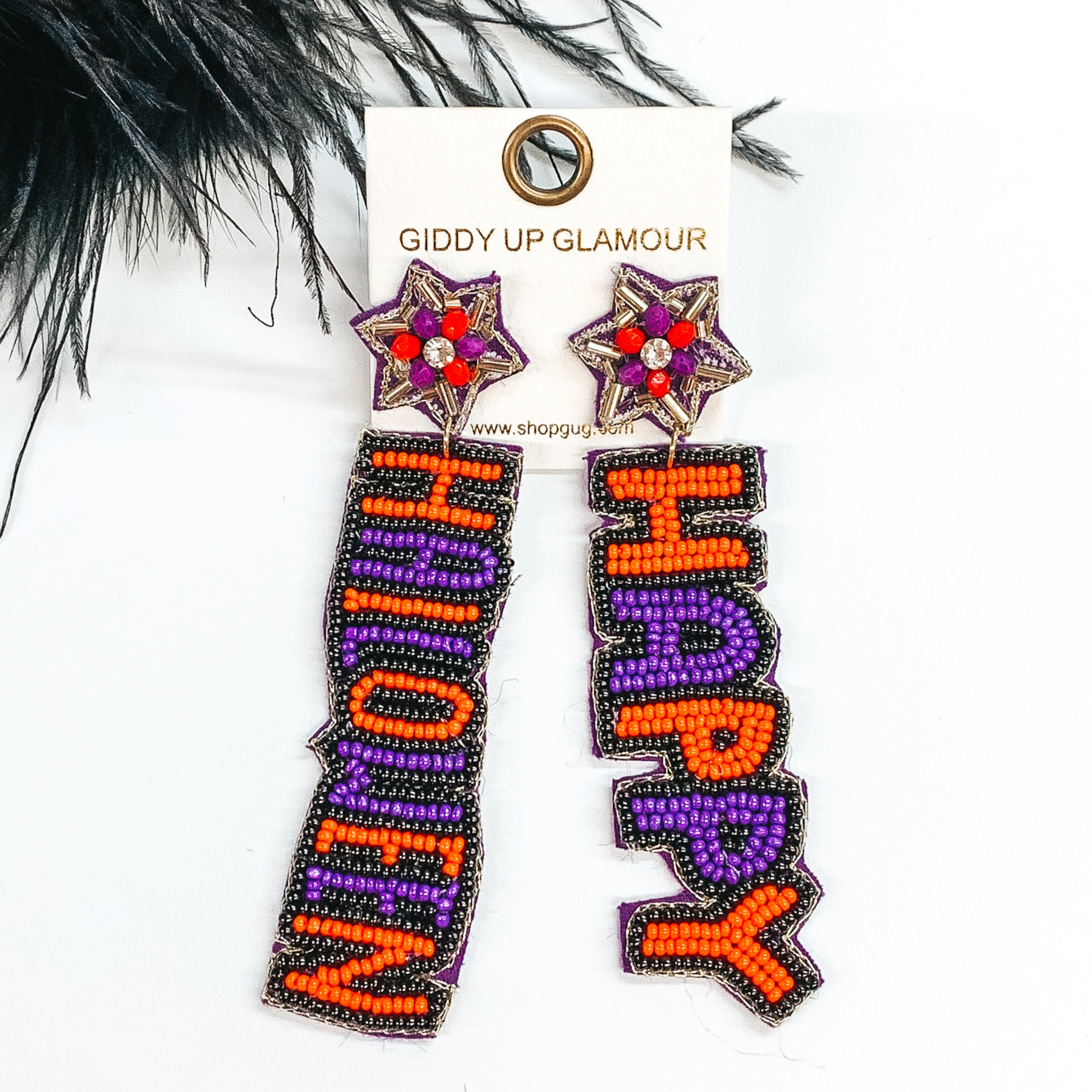 Star shaped post back earrings with  hanging beaded words. The words are "HAPPY" anf "HALLOWEEN" in orange and purple beads with a black beaded outline. These earrings are pictured on a white background with black feathers at the top. 