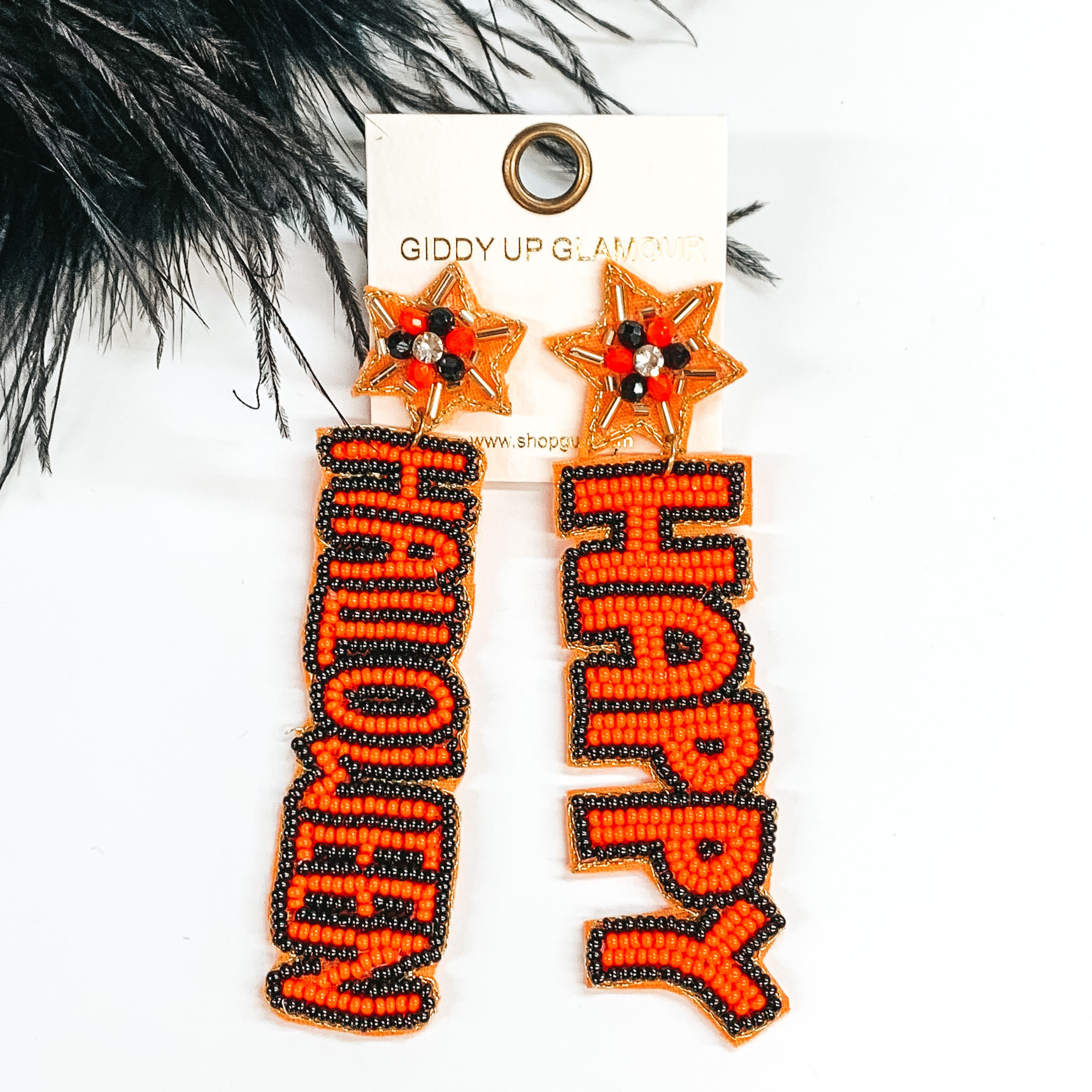 Star shaped post back earrings with  hanging beaded words. The words are "HAPPY" anf "HALLOWEEN" in orange beads with a black beaded outline. These earrings are pictured on a white background with black feathers at the top. 