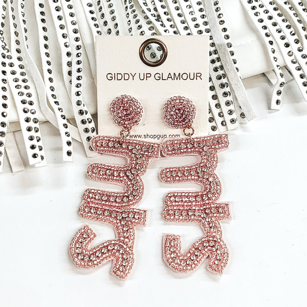 Pale pink beaded circle post earrings with a hanging beaded pendant. The pendant spells out "MRS" with a pale pink beaded outline and clear crystal inlay. These earrings are pictured on a white background and in front of crystal fringe.