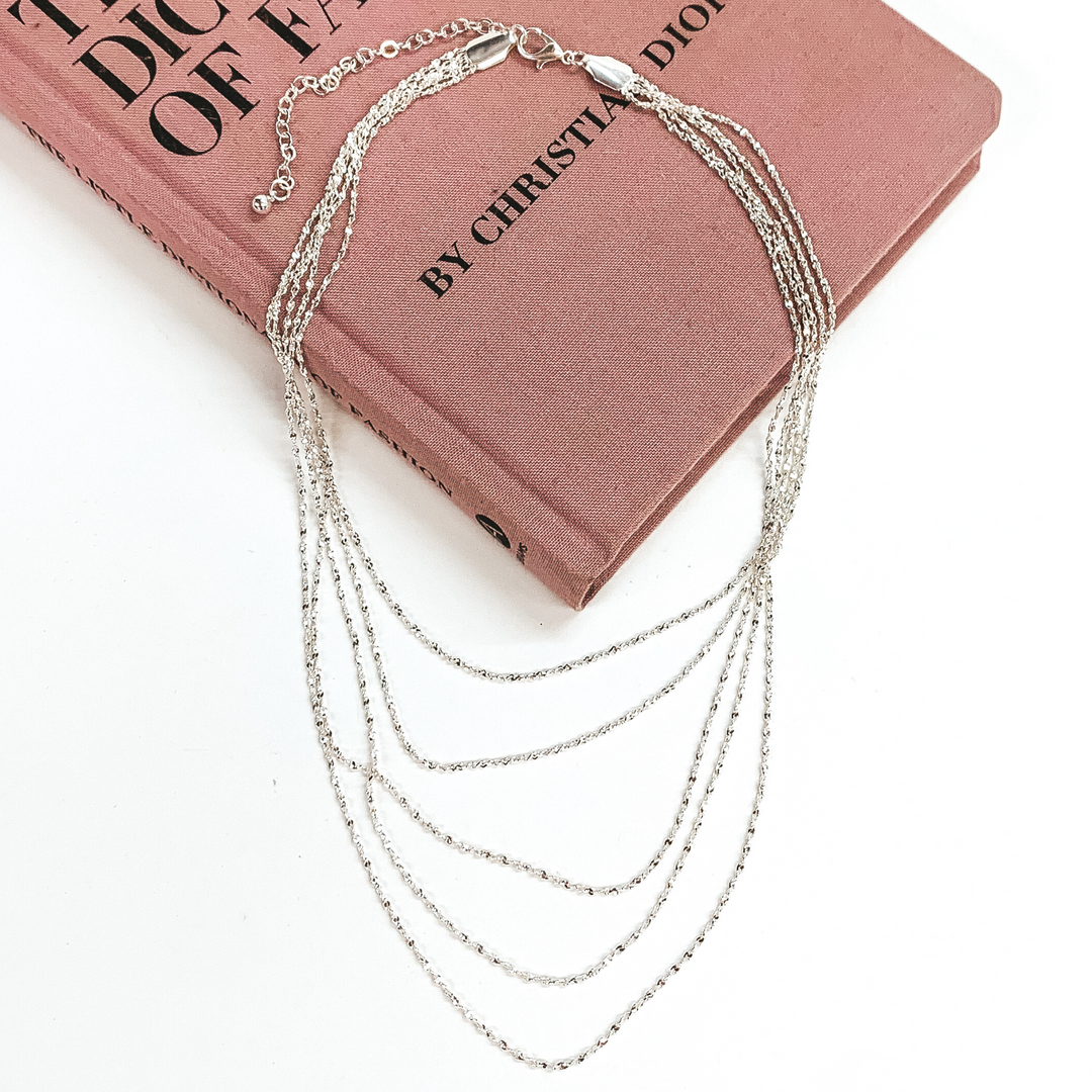 Five stranded silver chain necklace. This necklace is pictured laying on a pink book on a white background. 
