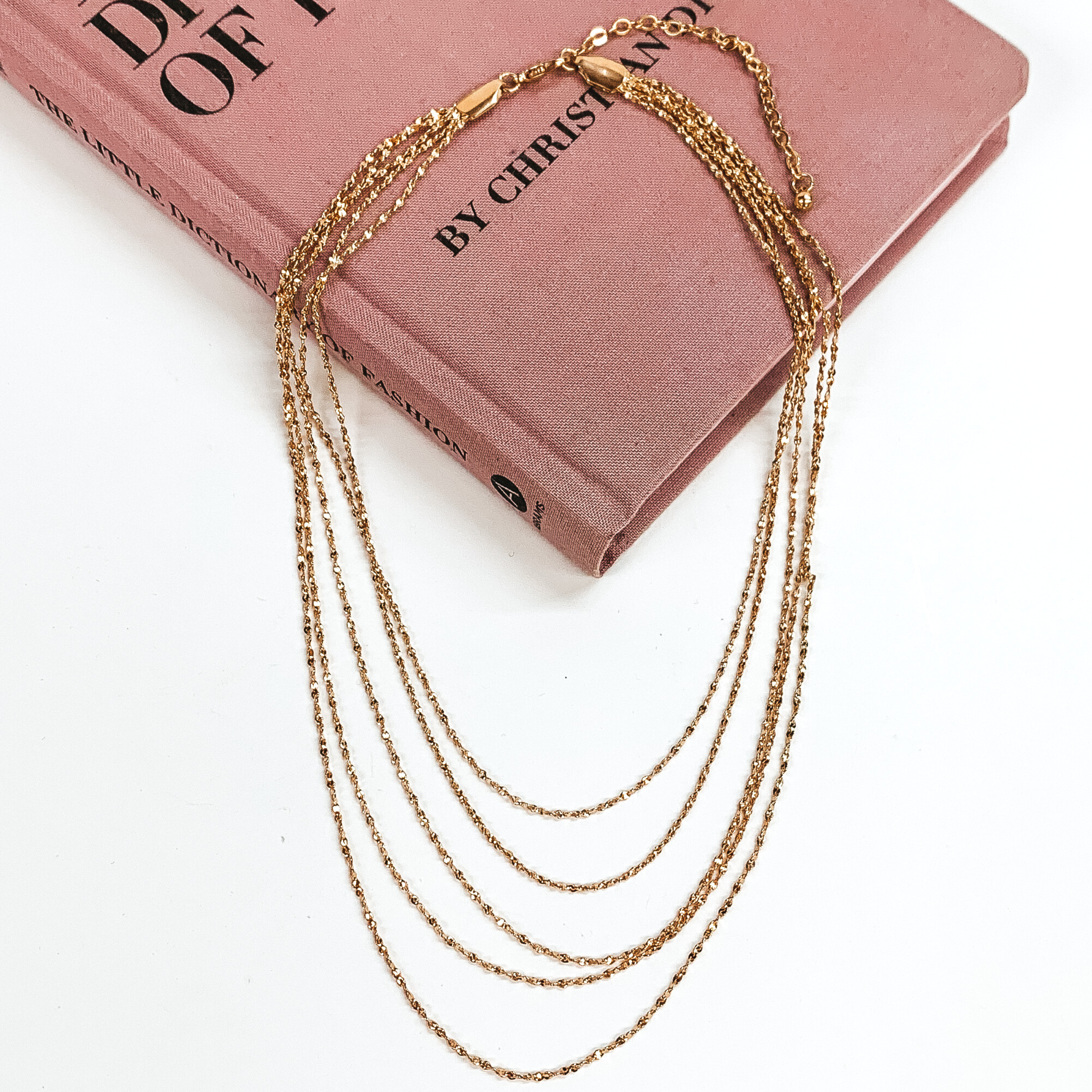 Five stranded silver chain necklace. This necklace is pictured laying on a pink book on a white background. 