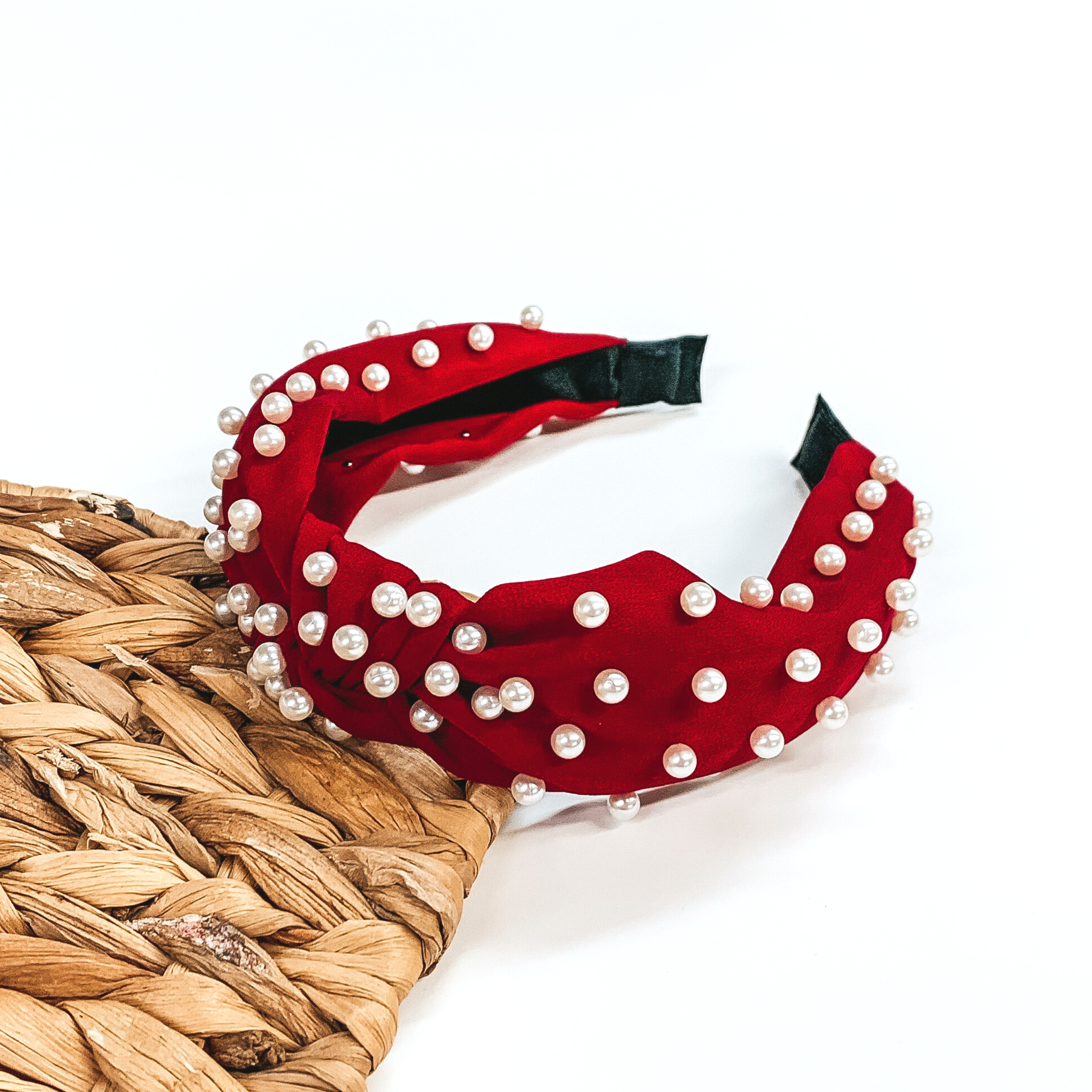 Dark red headband with white pearl accents. This headband is pictured laying partially on a basket weave board on a white background.