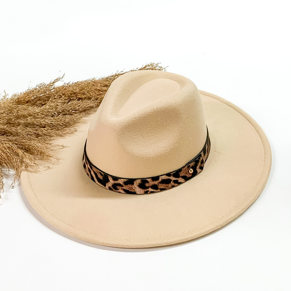 Ivory faux felt hat with a leopard print hat band. This hat is pictured on a white background with tan pompous in the background. 