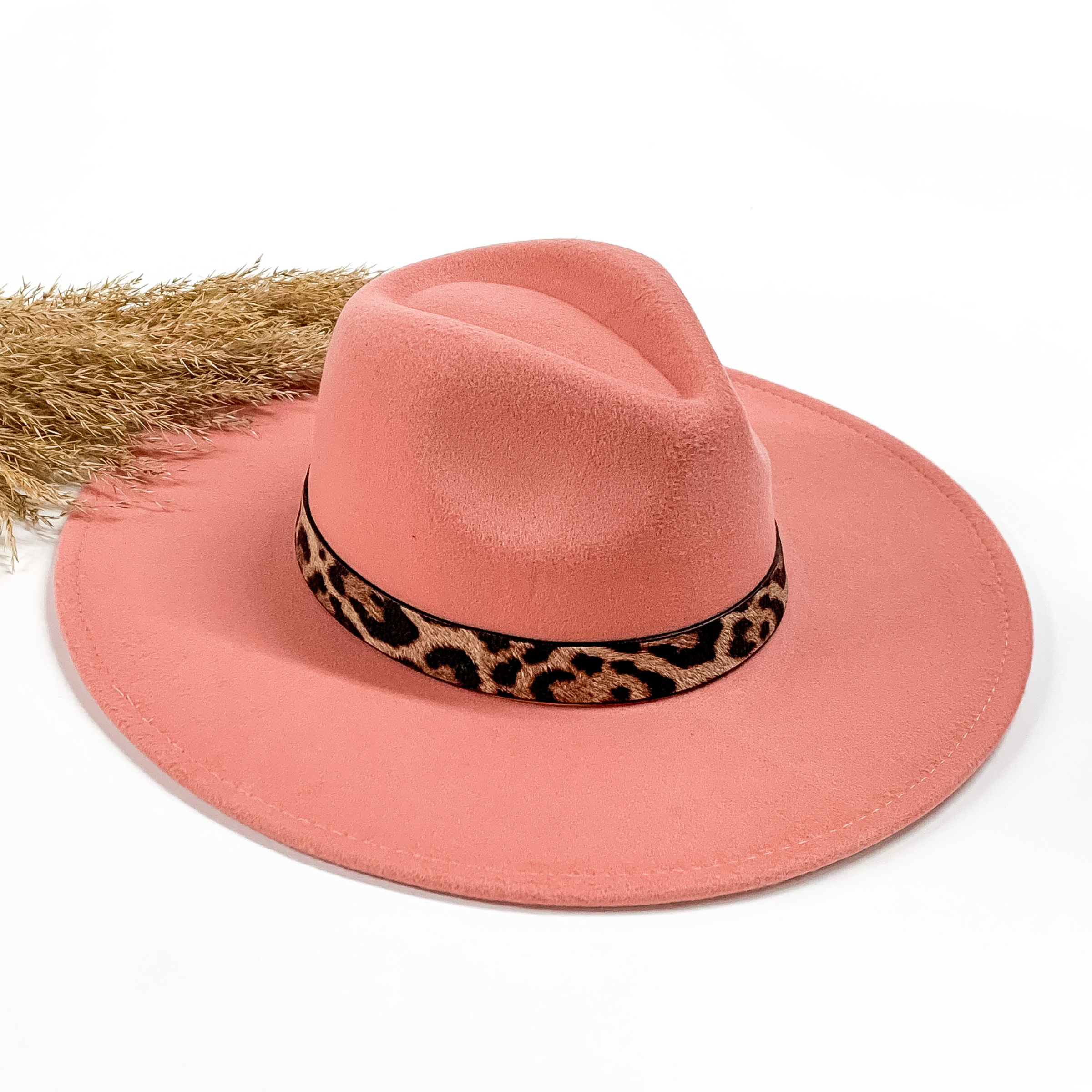Blush faux felt hat with a leopard print hat band. This hat is pictured on a white background with tan pompous in the background. 