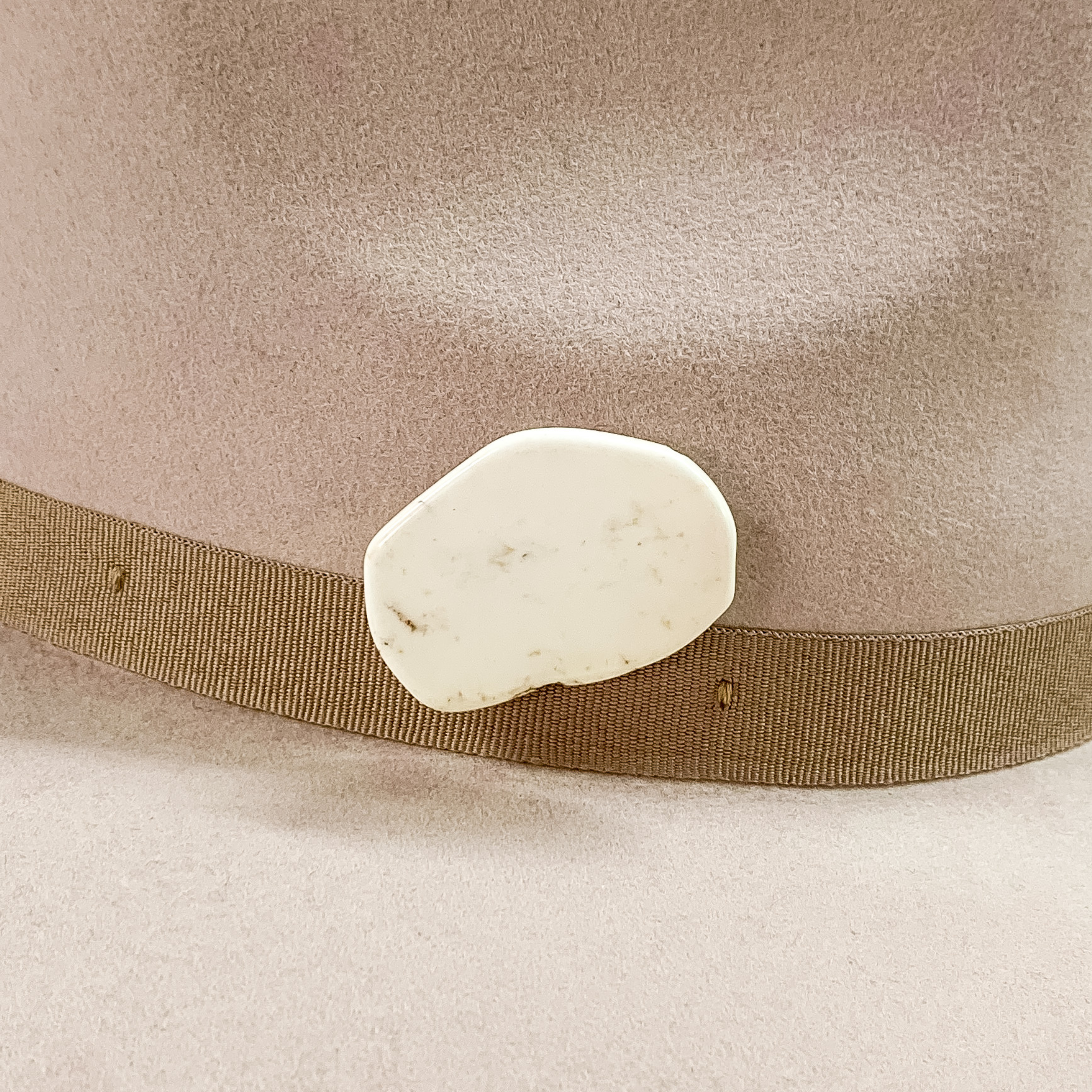 Ivory stone with an irregular shape hat pin pictured on a beige colored hat. 