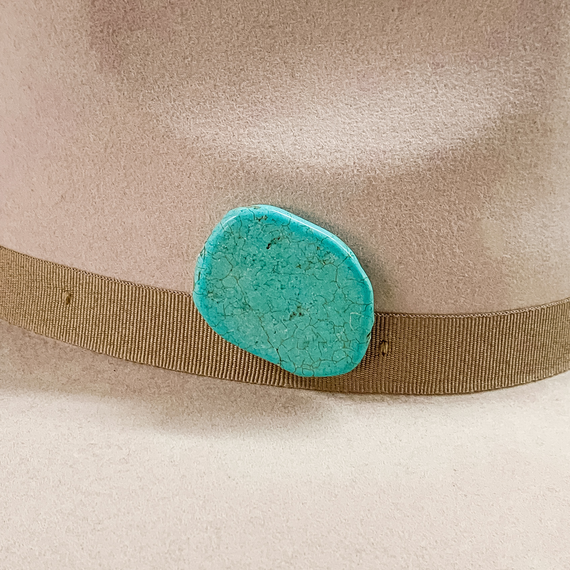 Turquoise stone with an irregular shape hat pin pictured on a beige colored hat. 