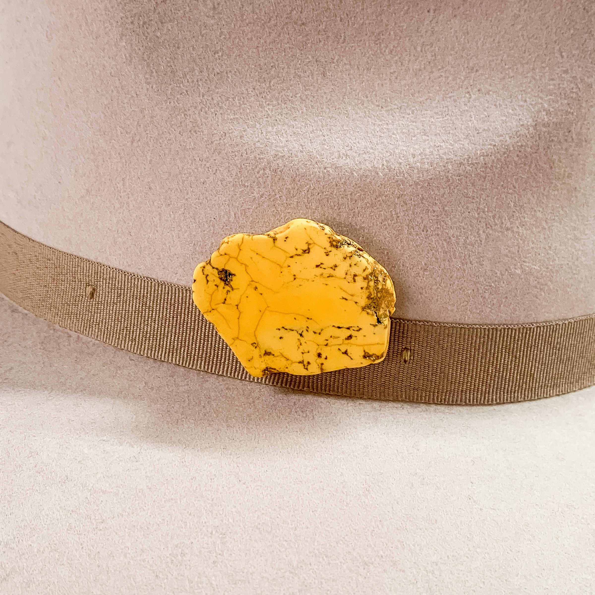 Yellow stone with an irregular shape hat pin pictured on a beige colored hat. 