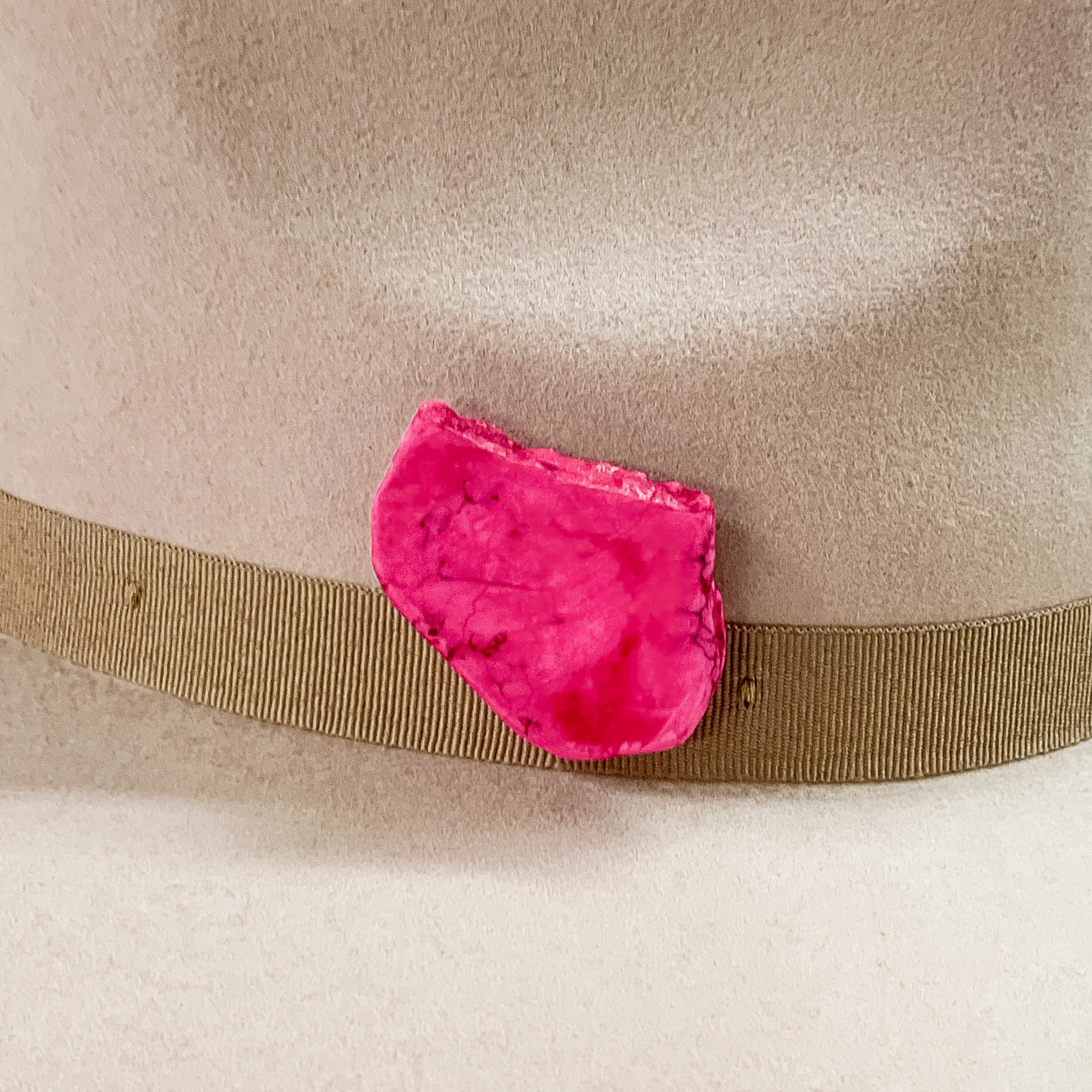 Pink stone with an irregular shape hat pin pictured on a beige colored hat. 