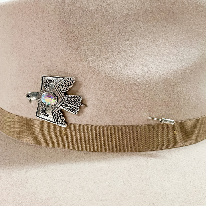 Silver, engraved thunderbird hat pin with an oval ab crystal in the center. This hat pin is pictured on a beige colored hat on a white background.