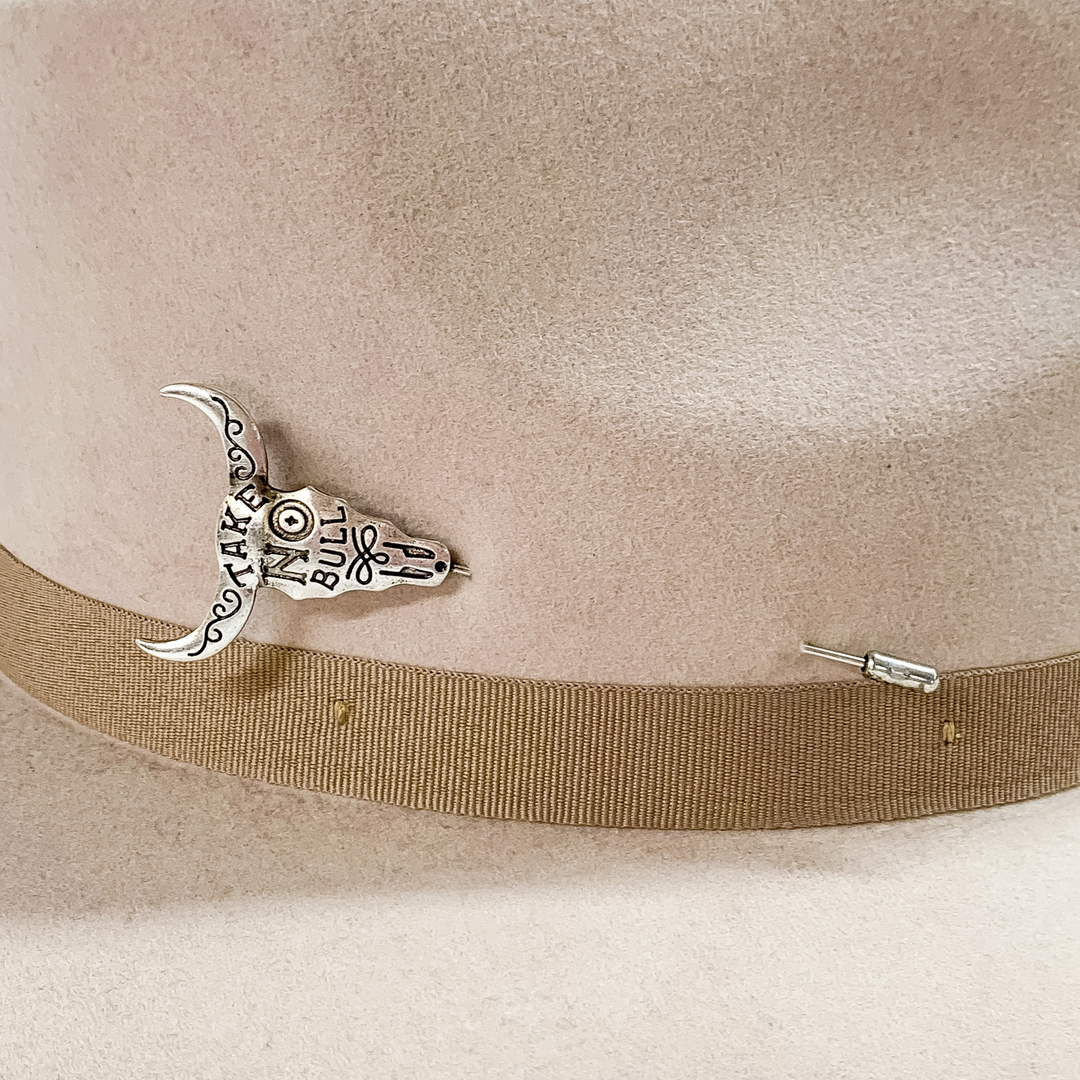 Silver bull skull hat pin with the words "TAKE NO BULL" engraved on the bull skull. This hat pin is pictured on a beige colored hat on a white background.