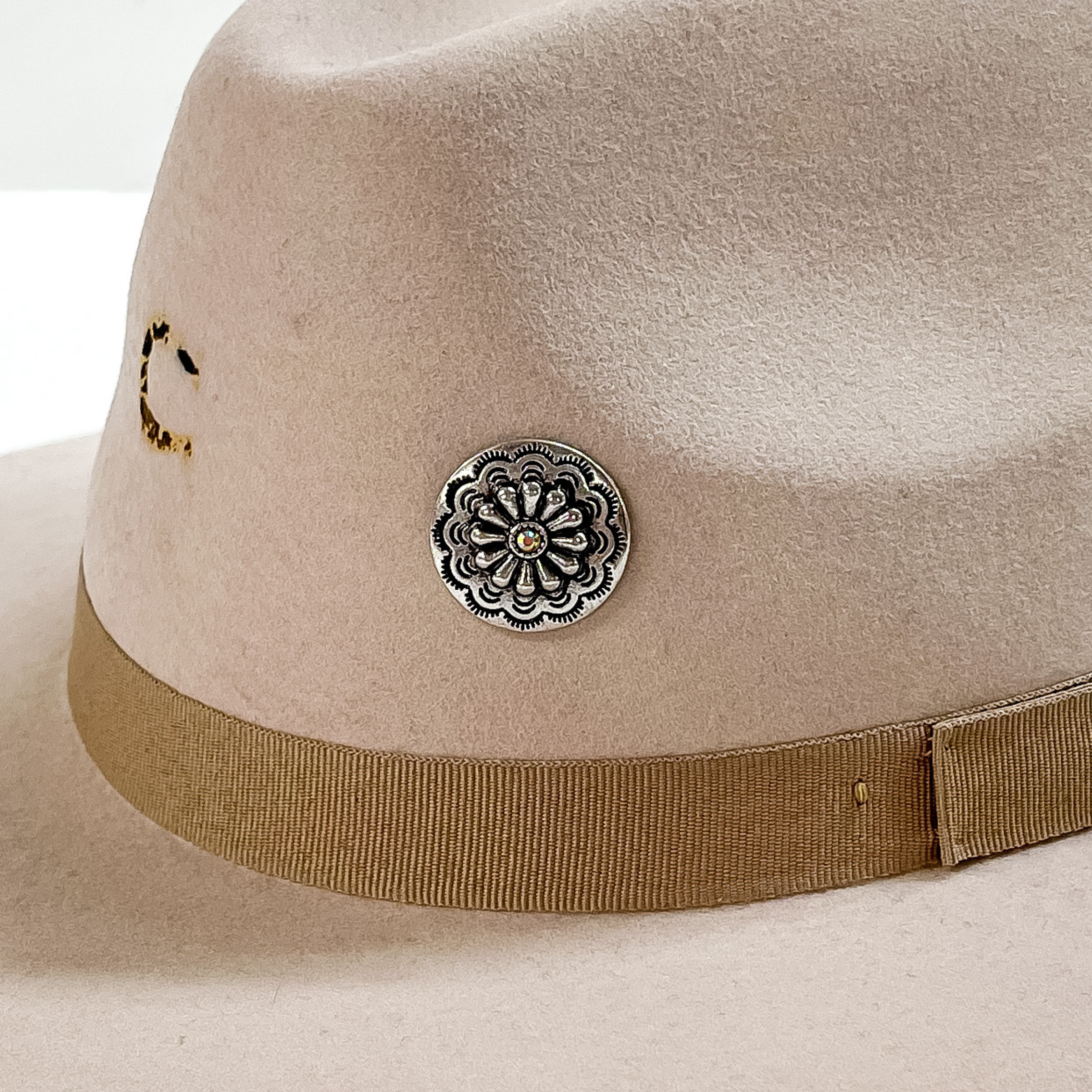 Silver, circle concho with detailed engraving and a small, center AB crystal hat pin. This hat pin is pictured on a beige hat and white background. 
