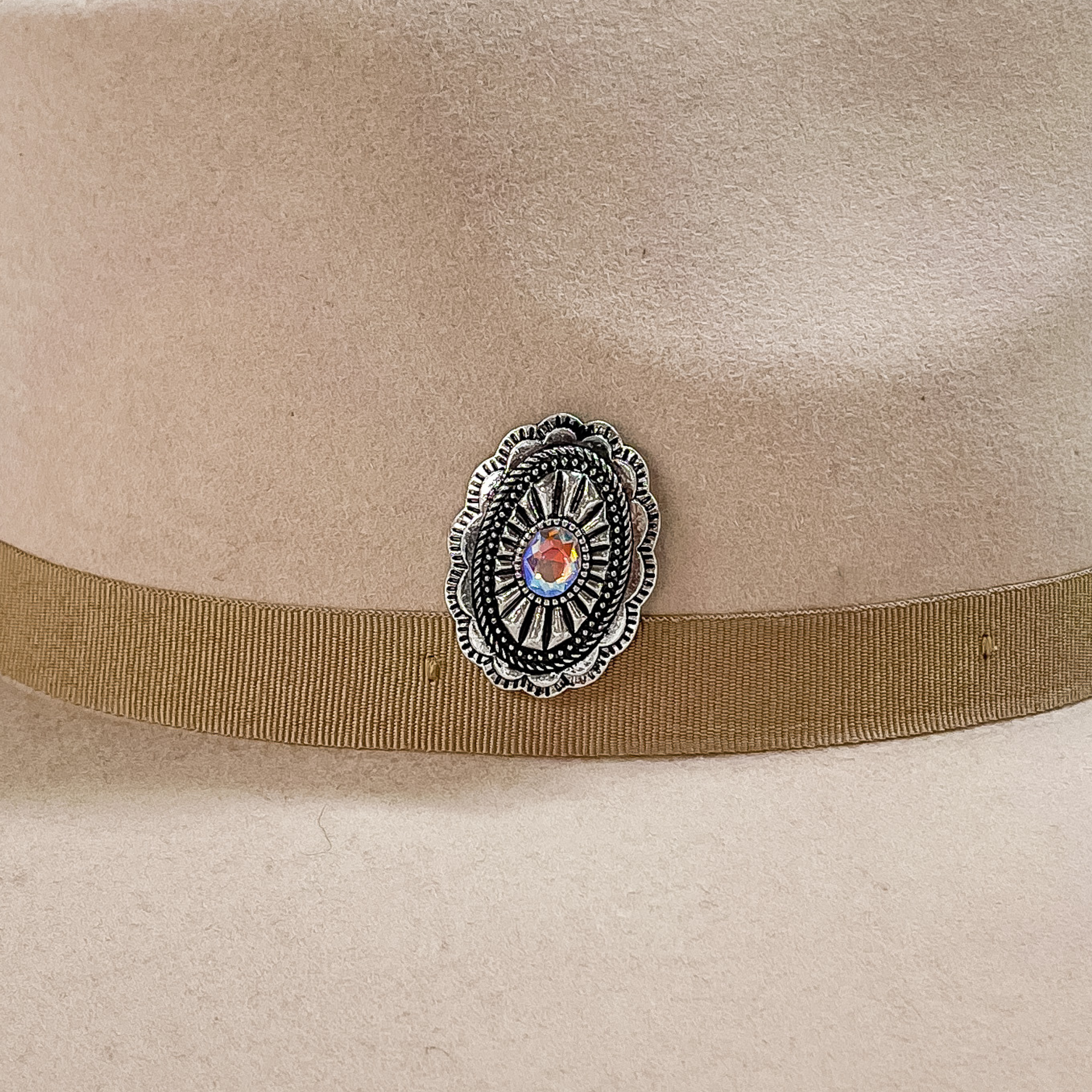 Silver, oval concho with detailed engraving and a center AB crystal hat pin. This hat pin is pictured on a beige hat. 