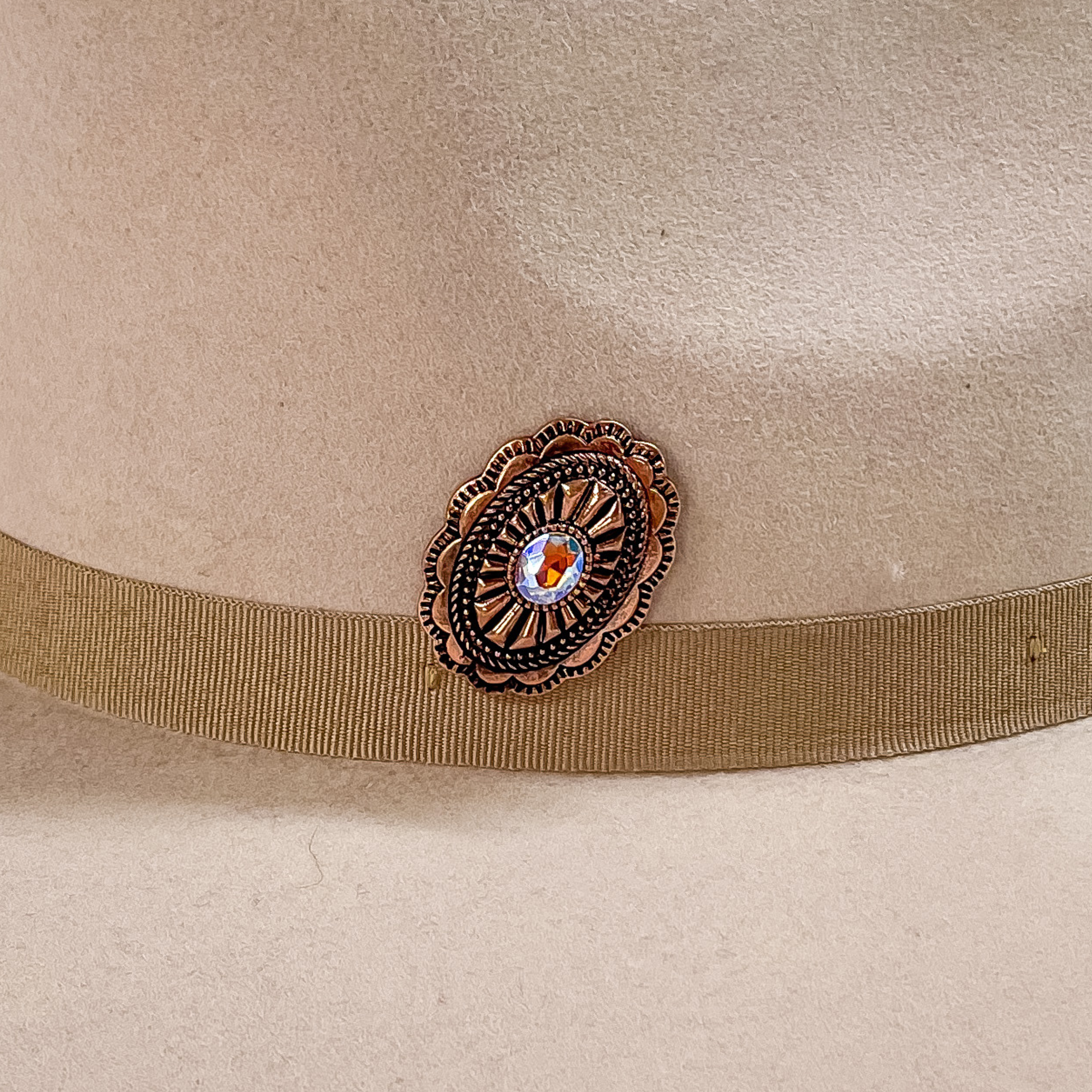 Copper, oval concho with detailed engraving and a center AB crystal hat pin. This hat pin is pictured on a beige hat. 