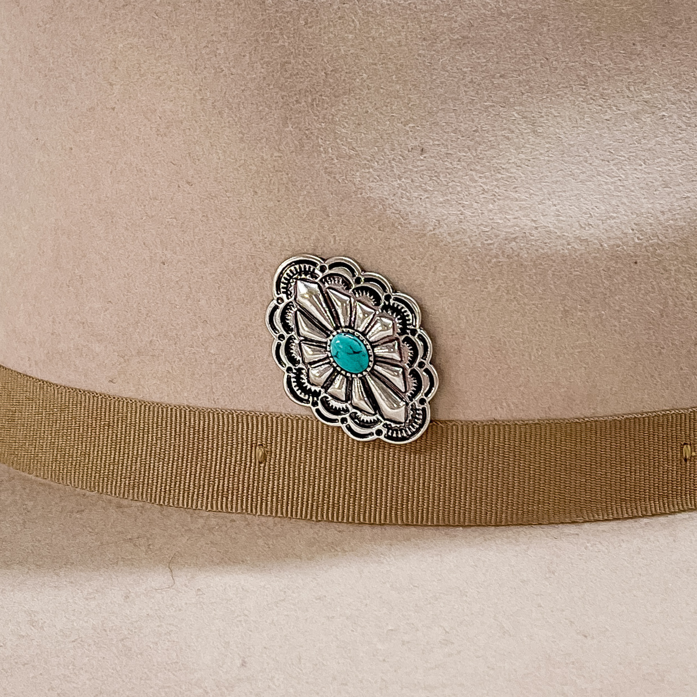 Silver, diamond concho with detailed engraving and a center turquoise stone hat pin. This hat pin is pictured on a beige hat. 
