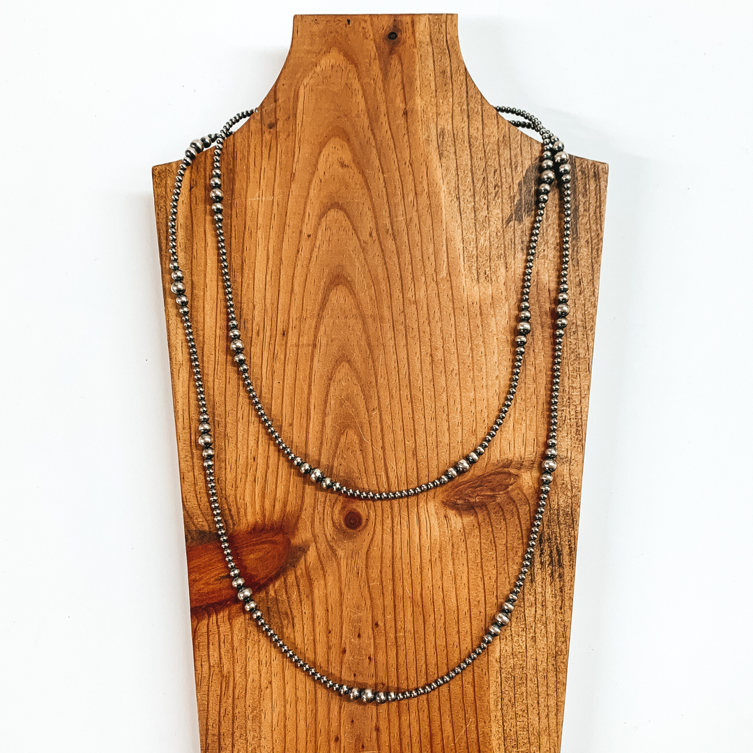 Silver beaded necklace wrpped around the necklace holder two times with graduated beaded spacers. This necklace is pictured on a brown necklace holder on a white background. Silver beaded necklace with graduated pearl spacers through out. This necklace is pictured on a brown necklace holder on a white background. 