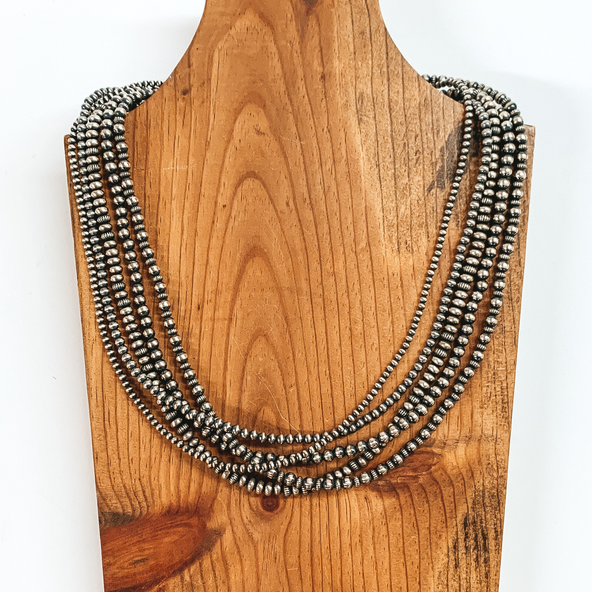Five strand silver beaded necklace with different design and size beads through out. This necklace is pictured on a brown necklace holder on a white background. 