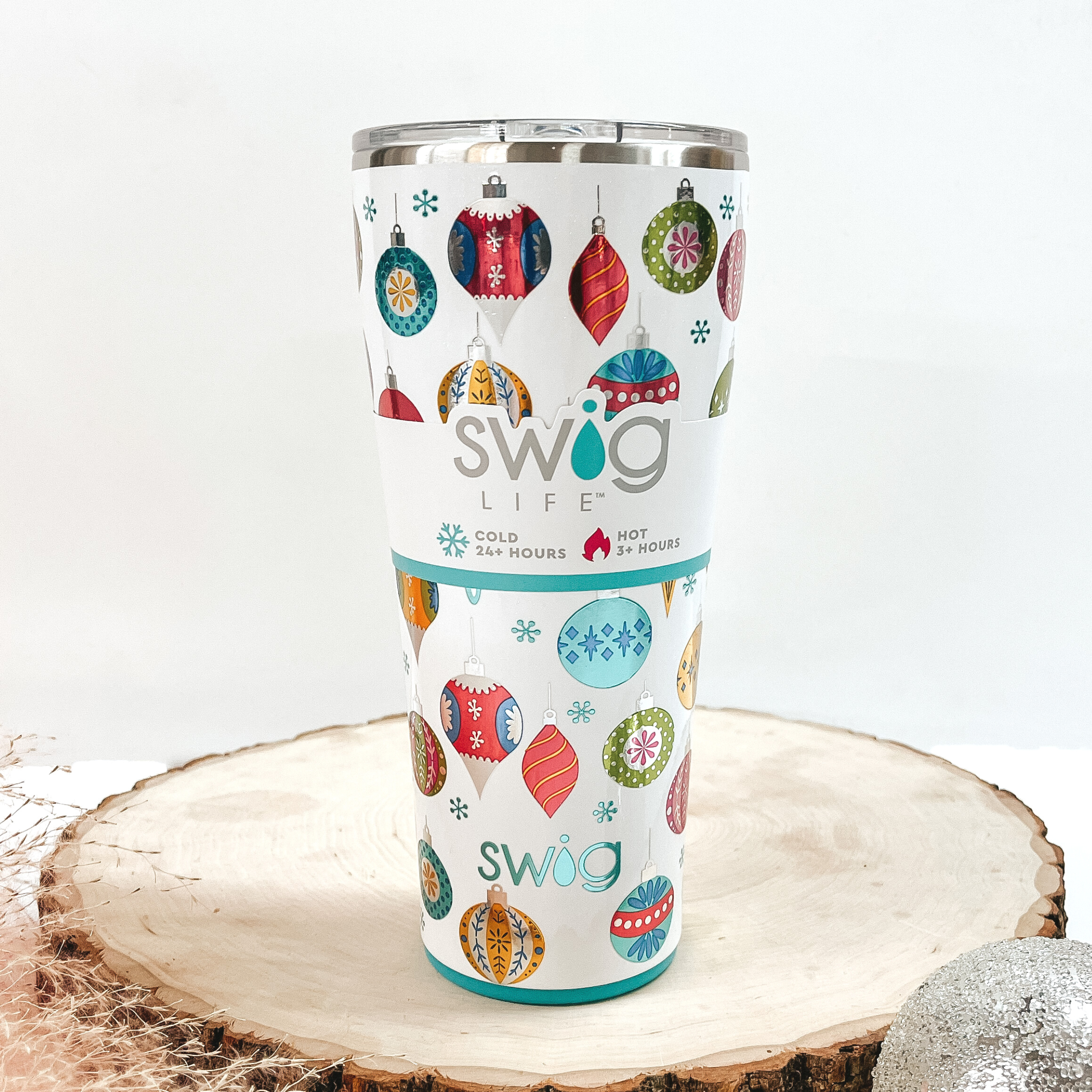White tumbler that has a multicolored and multishaped ornament print with a clear lid. This can cooler is pictured on a piece of wood on a white background.