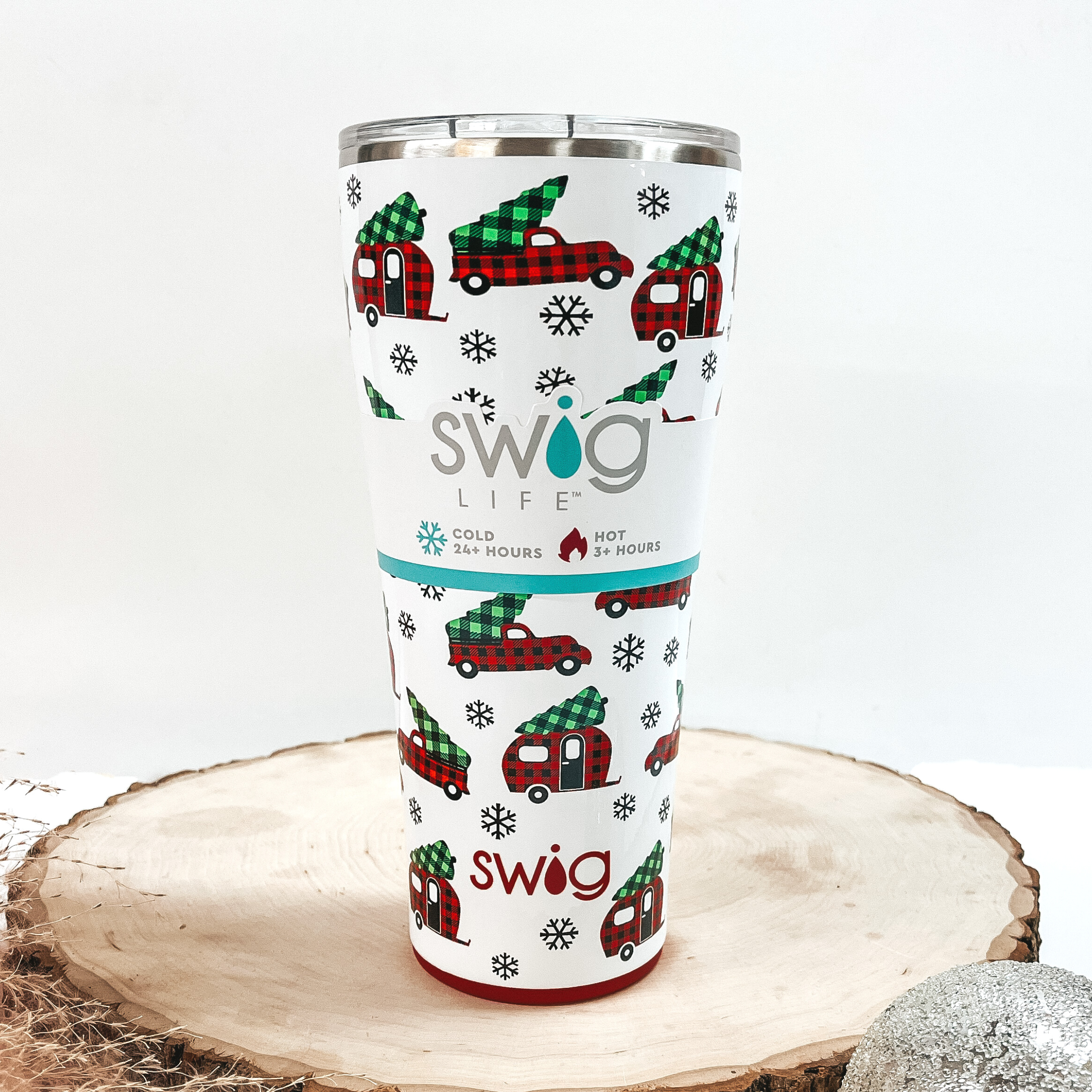 White tumbler that has a red buffalo plaid truck and green buffalo plaid tree print with a clear lid. This can cooler is pictured on a piece of wood on a white background.