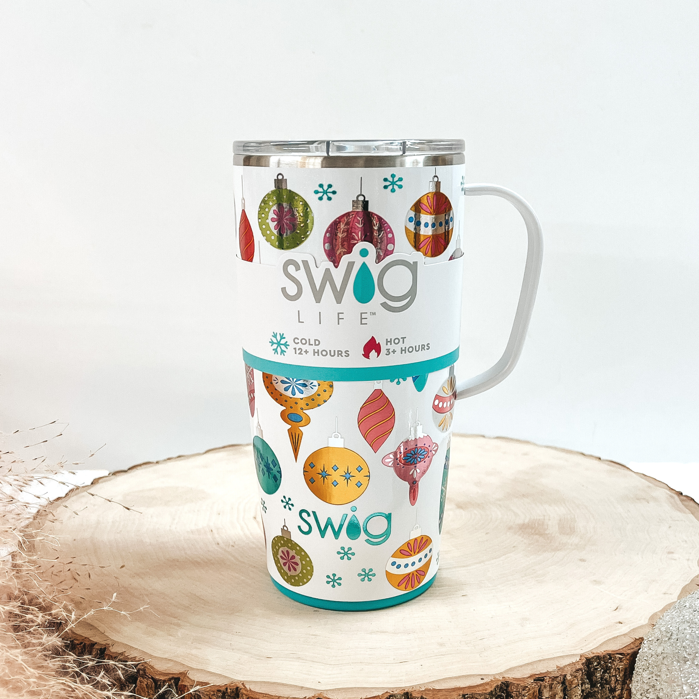 White mug that has a multicolored and multishaped ornament print with a white handle and clear lid. This can cooler is pictured on a piece of wood on a white background.