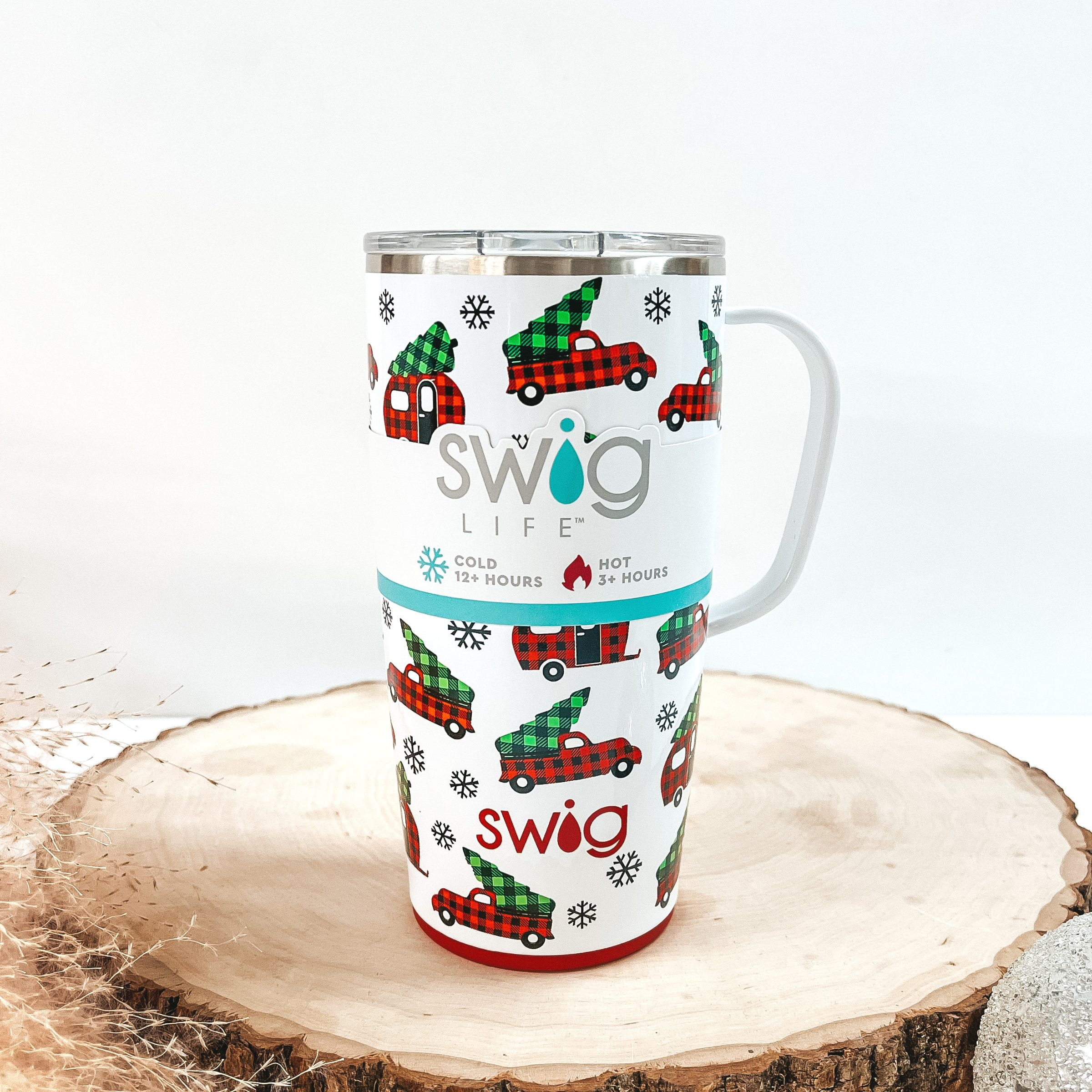 White mug that has a red buffalo plaid truck and green buffalo plaid tree print with a white handle and clear lid. This can cooler is pictured on a piece of wood on a white background.