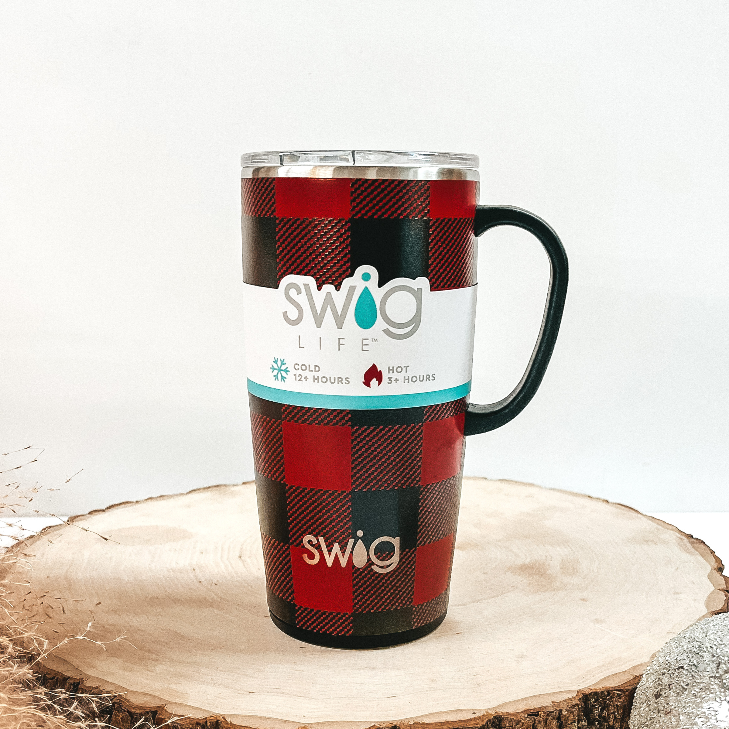 Red and black buffalo plaid mug with a black handle and clear lid. This can cooler is pictured on a piece of wood on a white background. 