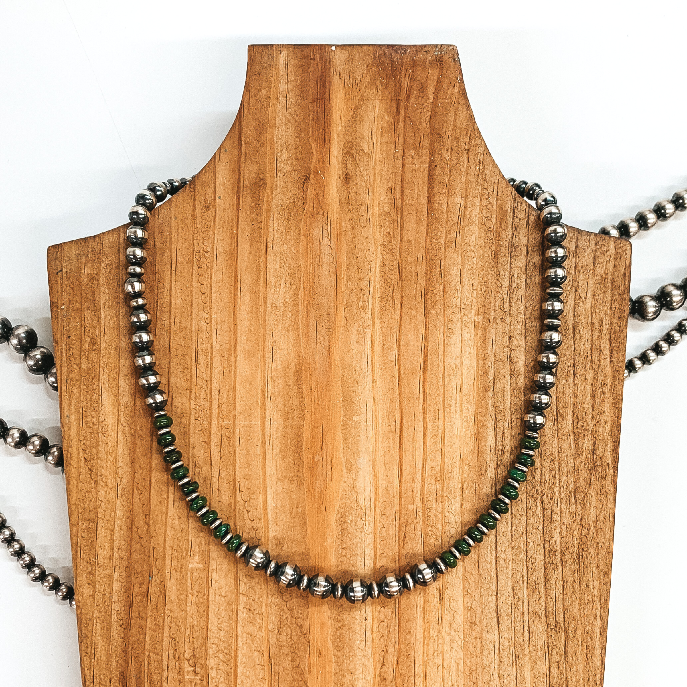 Silver beaded neckace with silver saucer spacers and turquoise bead spacers. This necklace is pictured laying on a wood necklace holder on a white background.
