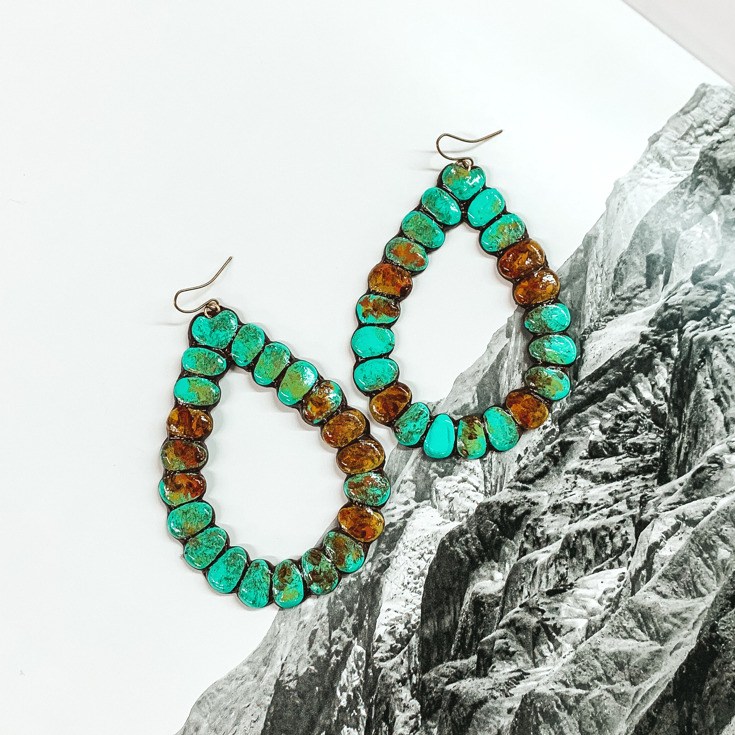 Open teardrop earrings in turquoise and tan. These earrings are pictured on a black and white mountain picture. 