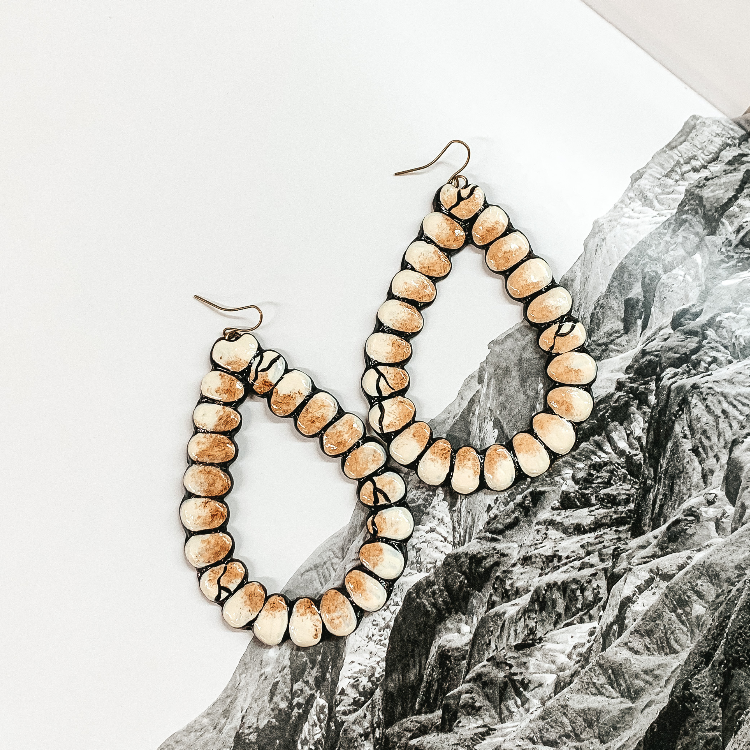 Open teardrop earrings in ivory and tan. These earrings are pictured on a black and white mountain picture. 