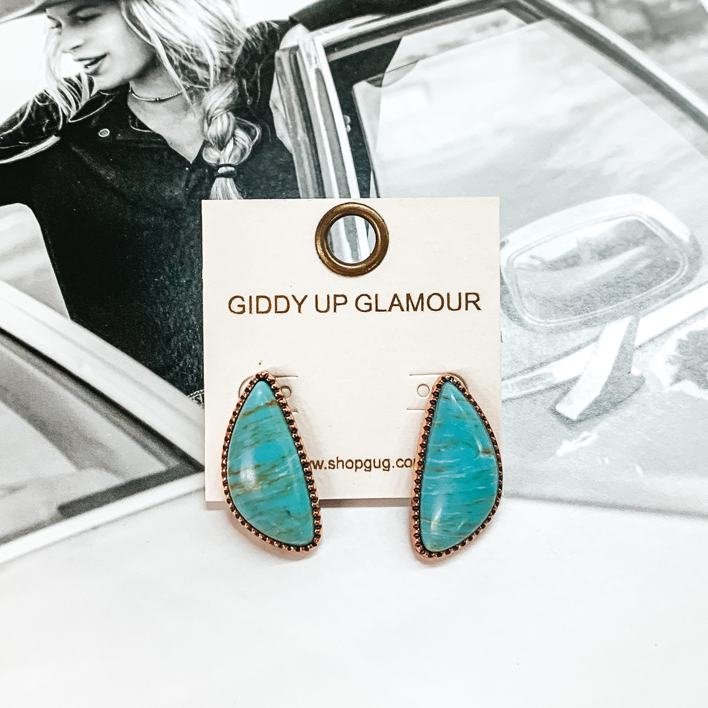 Irregular shaped turquoise stone stud earrings with a copper backing. These earrings are pictured on top of a black and white picture of a girl in a car. 